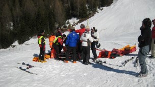 Several people and medical personel in a skiing slope, with stretchers, helping a person.