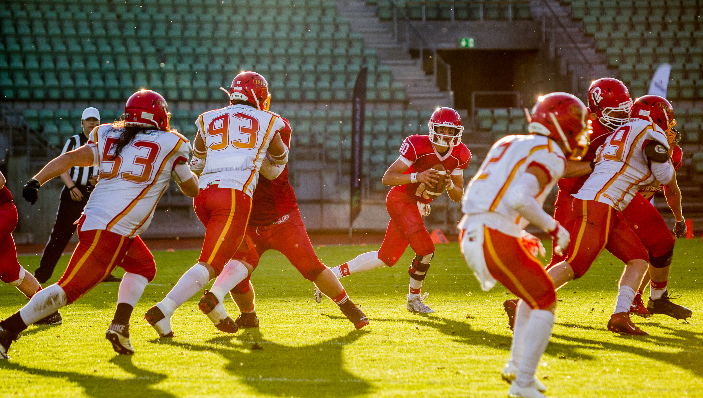 Several american football players on in a match, one player with the ball, several players arund the field.