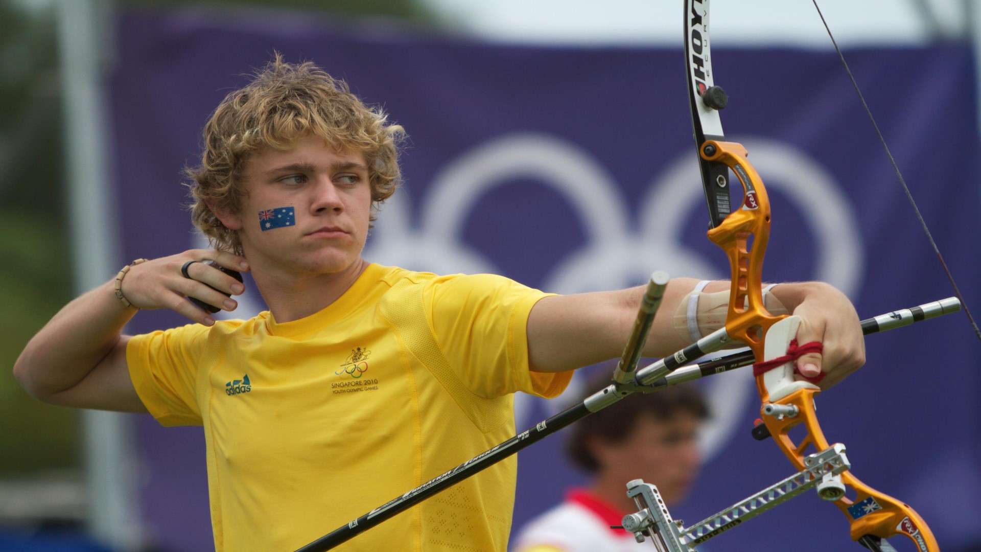 Archer looking forward, having just released his arrow, holding on to the bow with his left arm.