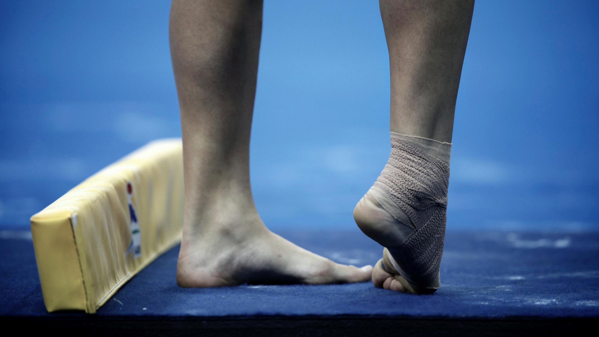 Close-up of legs and feet of a gymnast, one foot on the ground the other foot slightly lifted with toes touching the ground.