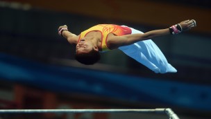 Gymnast in a competition in the air, moving backwards with his body and arms out to the side.