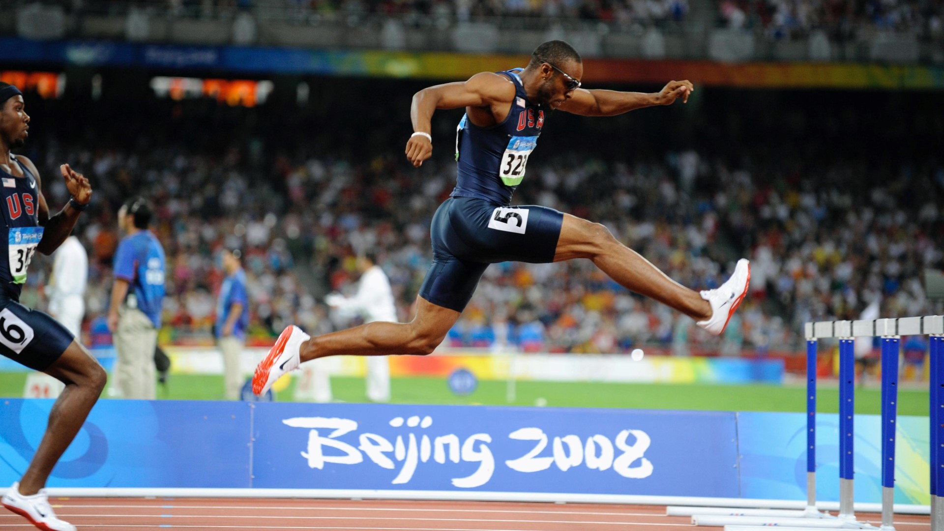 Athlete on the track and field during a competition, in the air getting ready to jump over a hurdle.