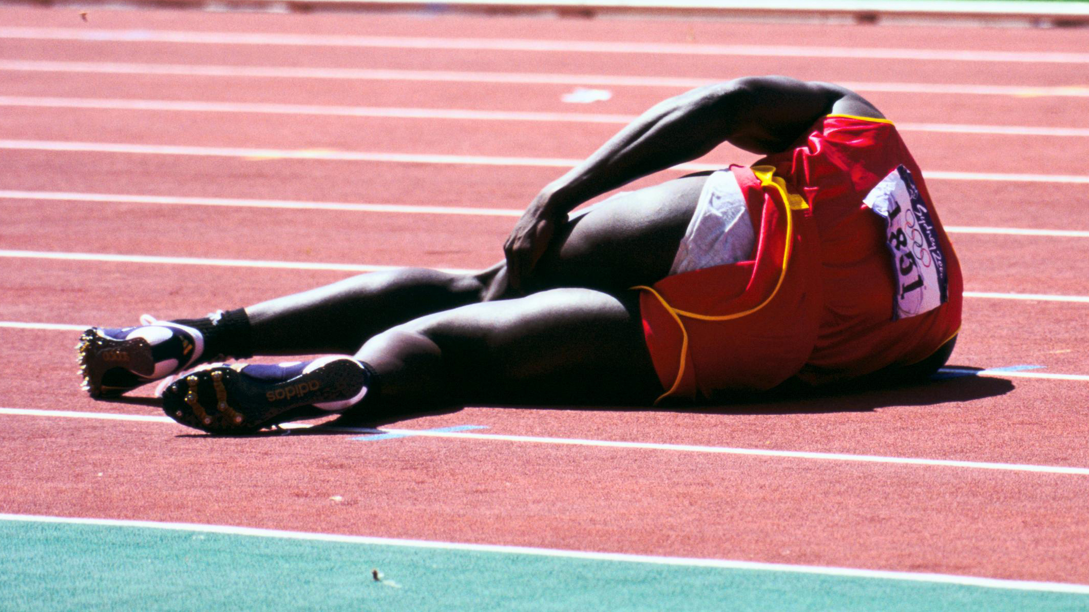 Athlete lying on the track and filed, his left hand is on his thigh.