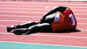 Athlete lying on the track and filed, his left hand is on his thigh. 
