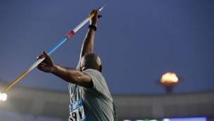 Athlete holding a javelin behind him with both hands at a stadium.