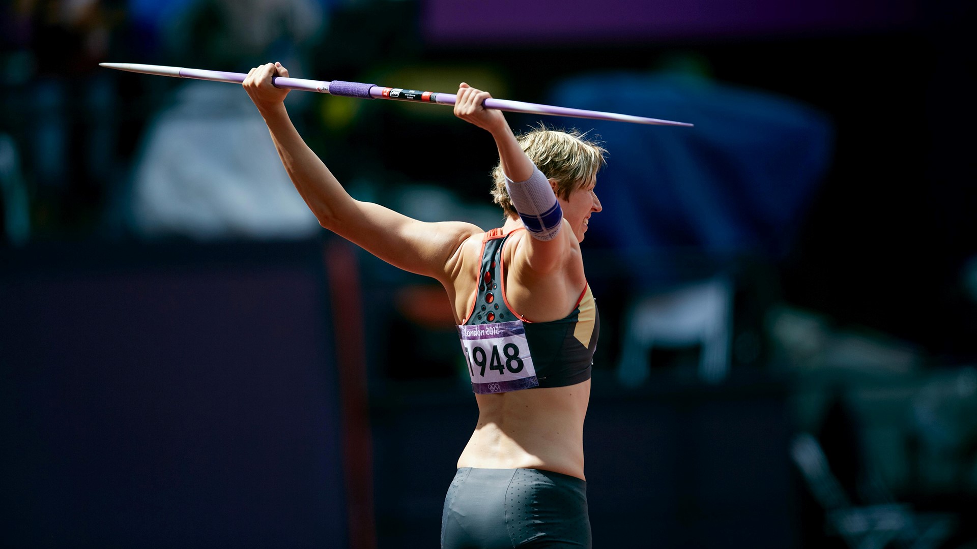 Athlete holding the javelin behind her back, up with both arms, looking forward.