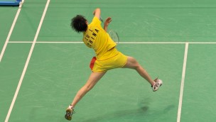 Badminton player one the court seen from behind. Athlete in the air trying to hit with the racket.