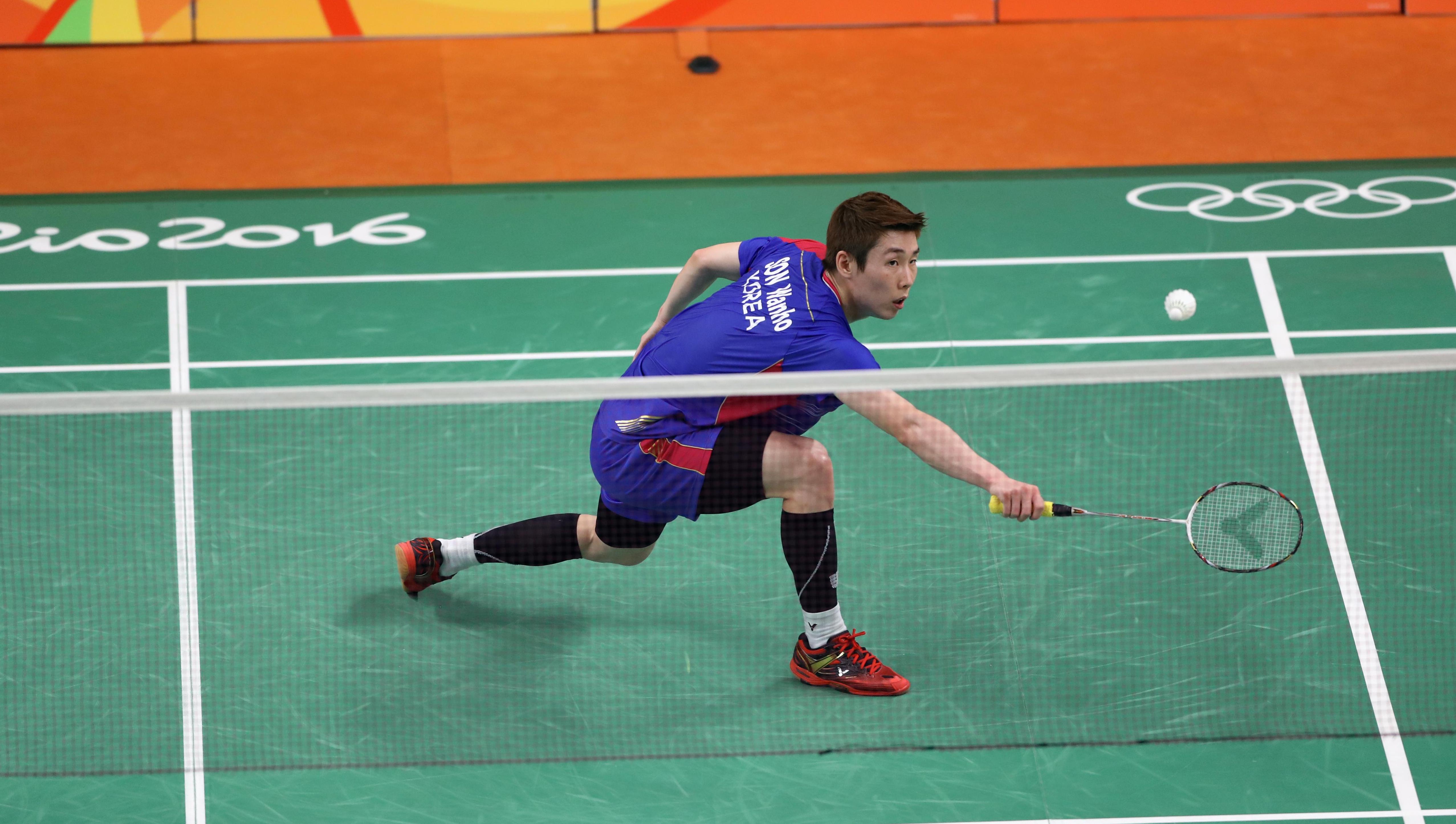 Player reaching for the feather-ball, stretching his right arm out with the racket in his hand, eyes on the light feather-ball.