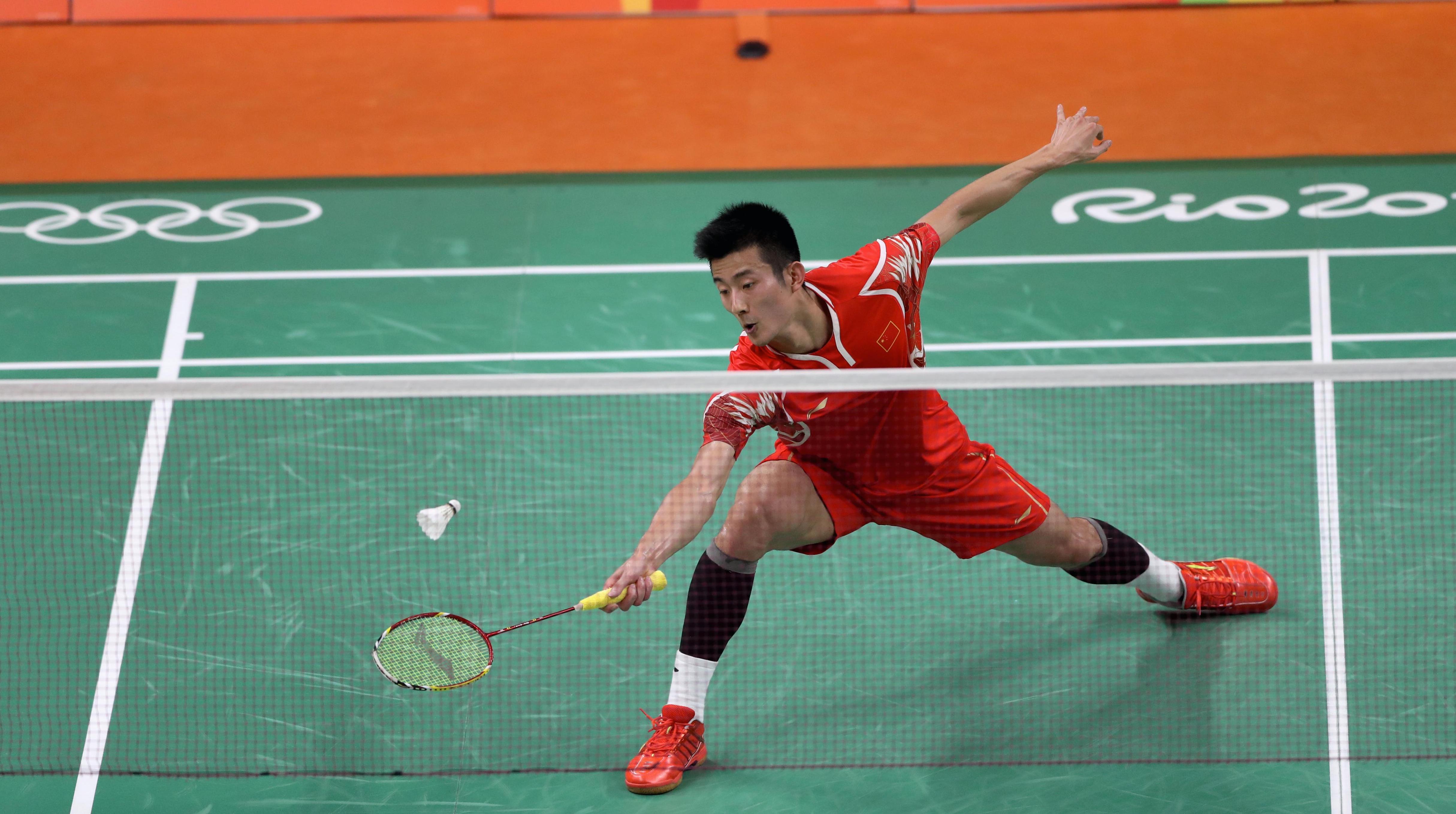 Badminton player on the court trying to cath the fly-ball with his racket. Arm stretched out, one leg stretched out in front of the other.