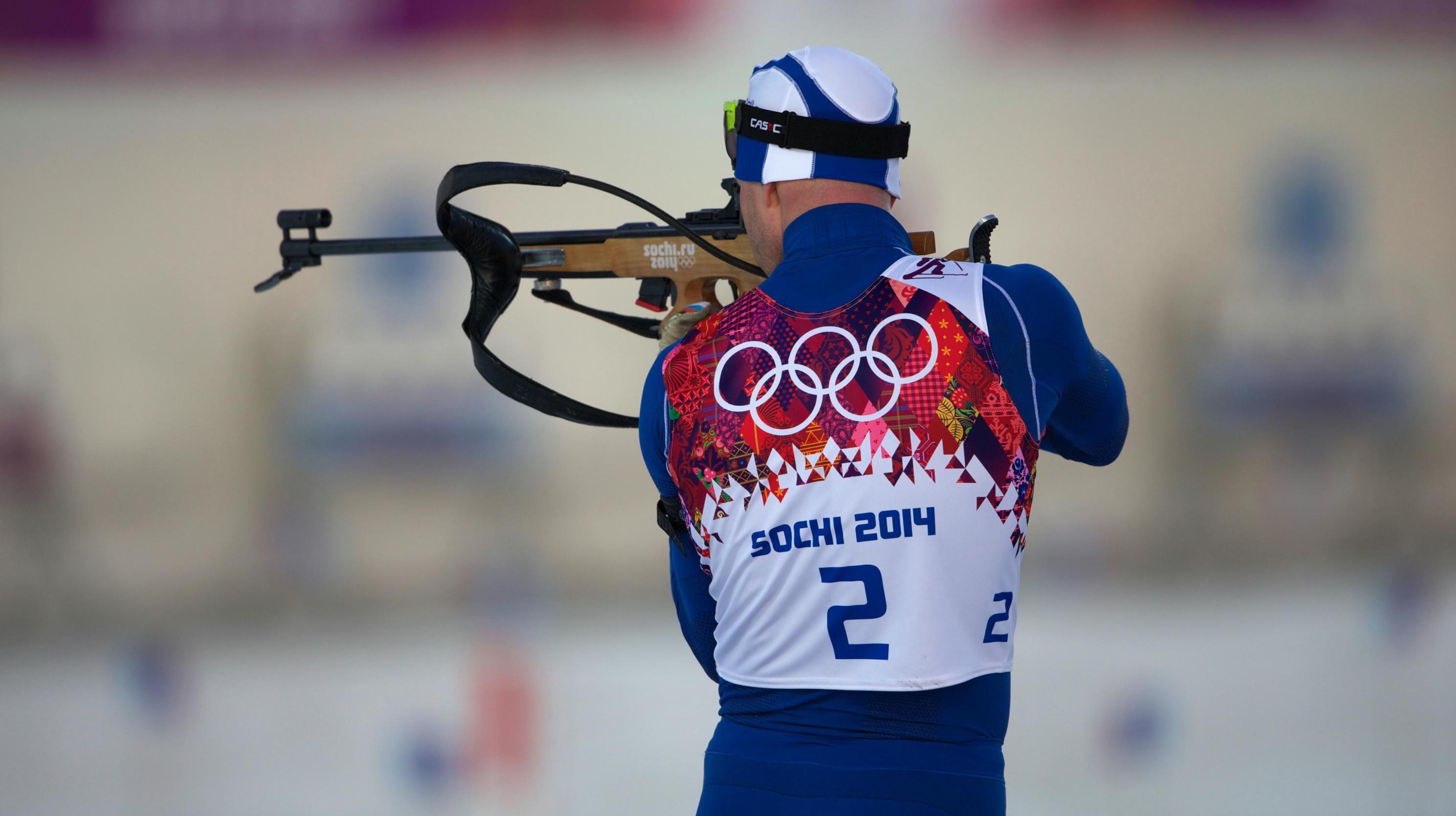 Athlete in an Olympic competition, standing and aiming at the target, holding the rifle up to his face, aiming.