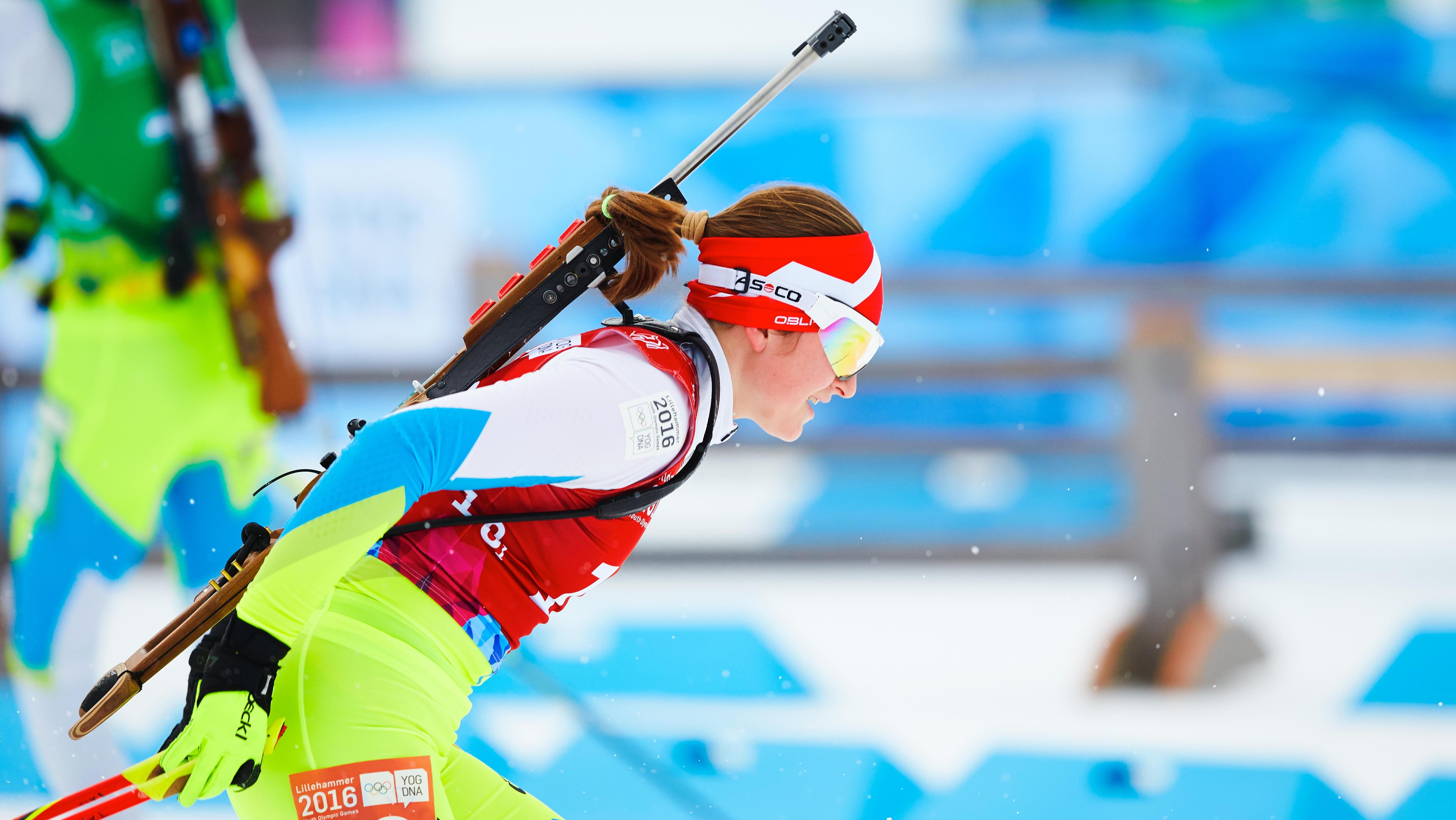 Athlete seen from the side during a competition doing cross-country skiing, with her rifle on her back.