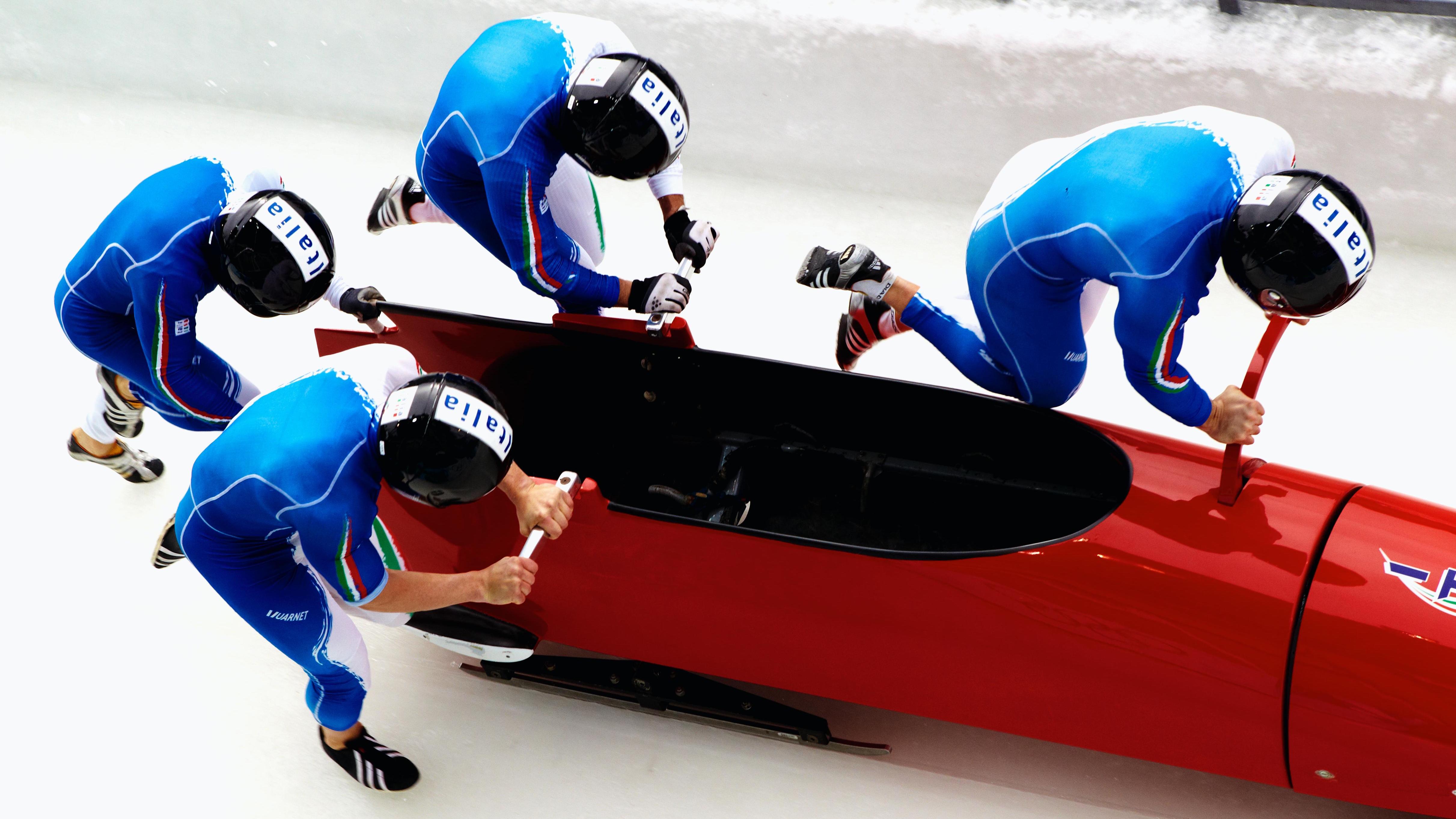 Start of a race, seen from above, 4 athletes running and holding onto the bobsleigh.