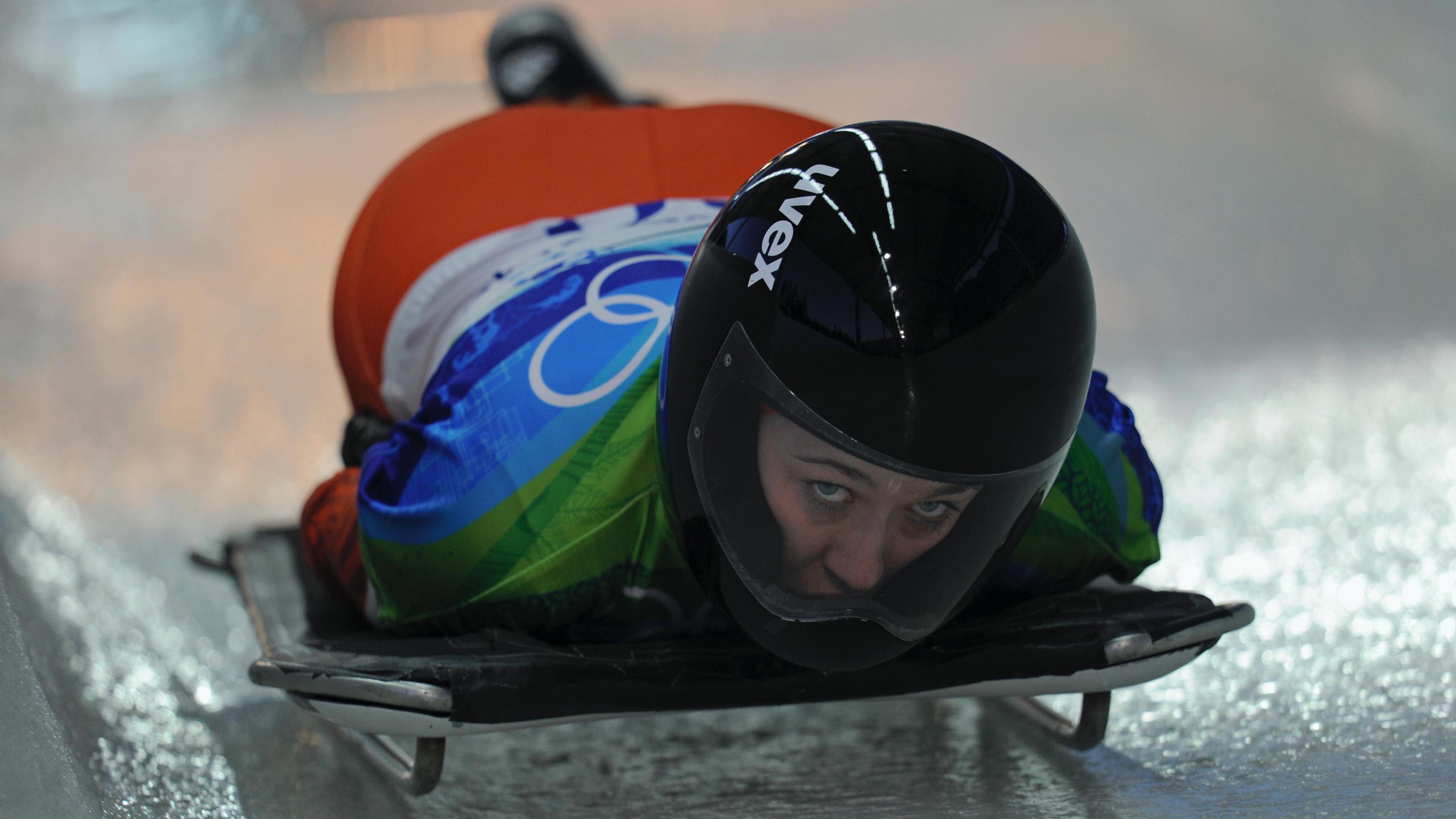 Athlete lying on the skeleton, arms to the side, helmet on, eyes forward.