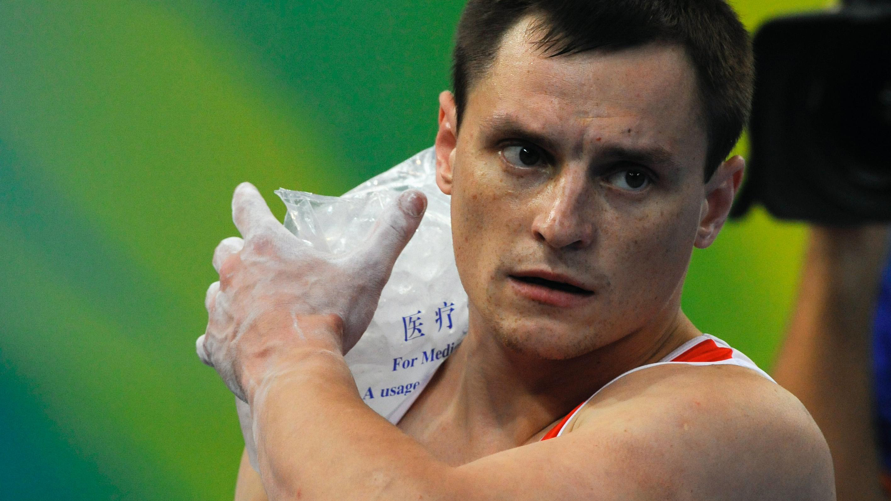 Athlete with a ice-pack on his shoulder, using his left hand to hold it in place.