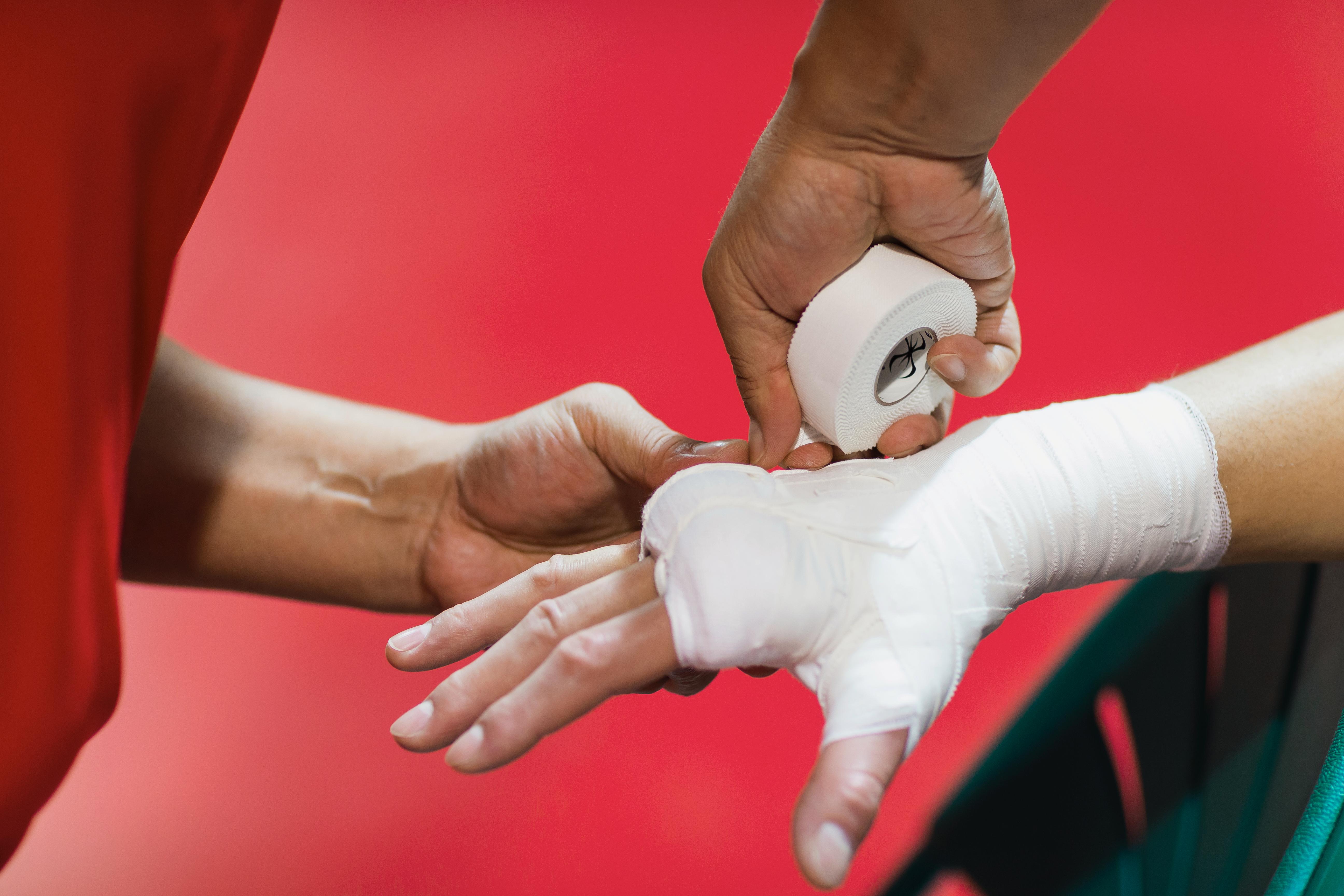 Close up of a hand that is being taped ariund the wrist and some of the fingers by a physician.