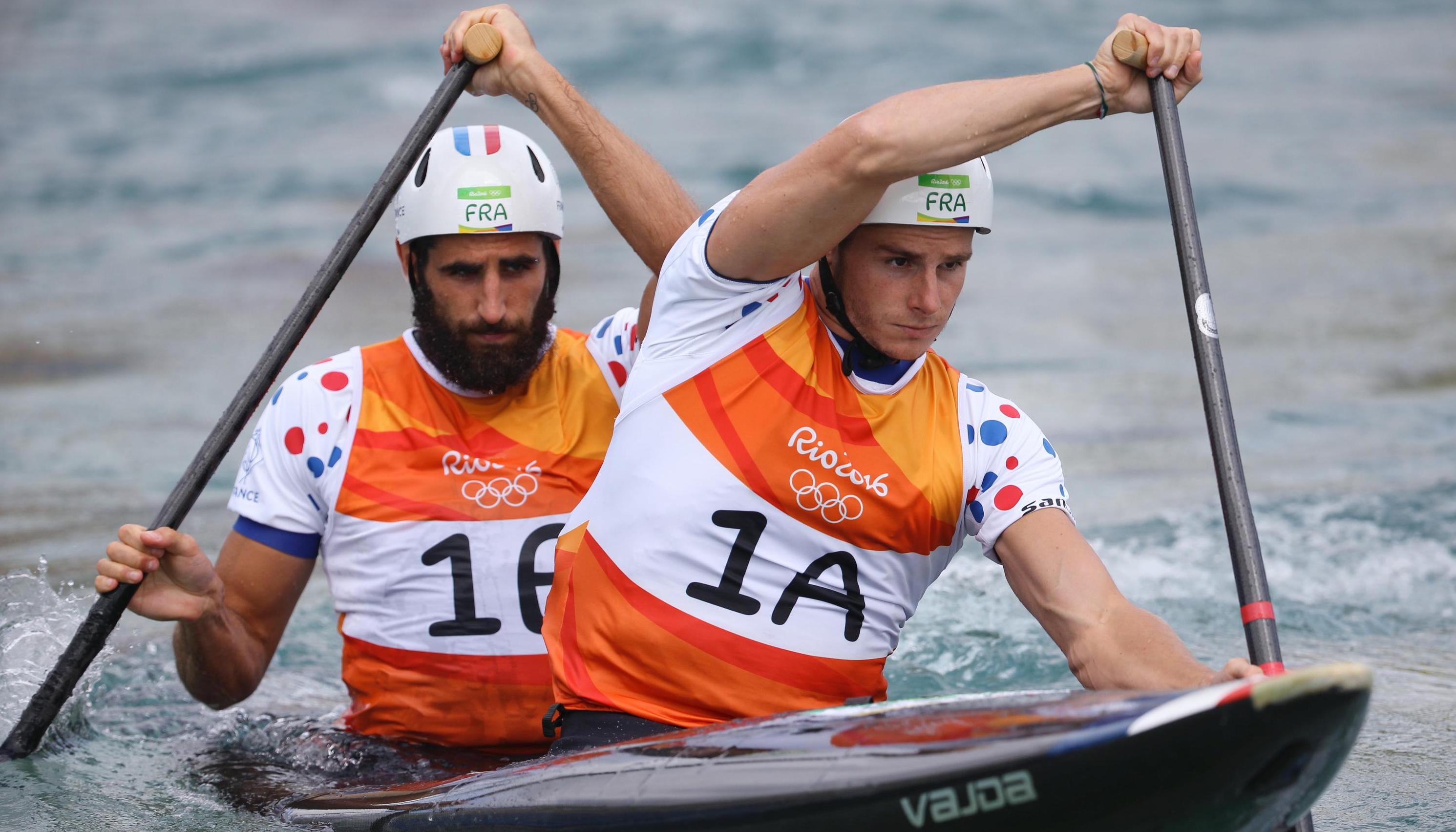 Two athletes in a kayak during an Olympic competition, paddling on each side.
