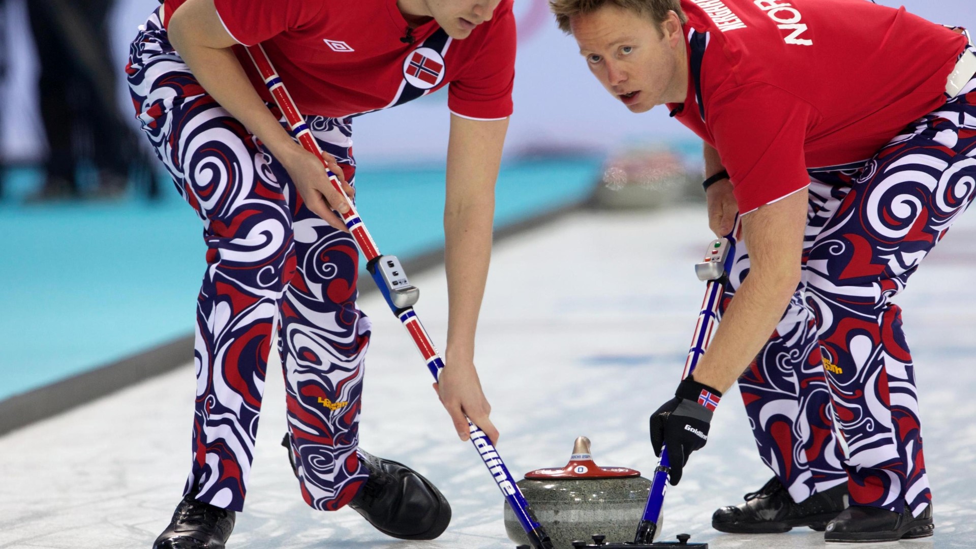 Two curlers on the ice with broomsticks in front of the curling-stone.