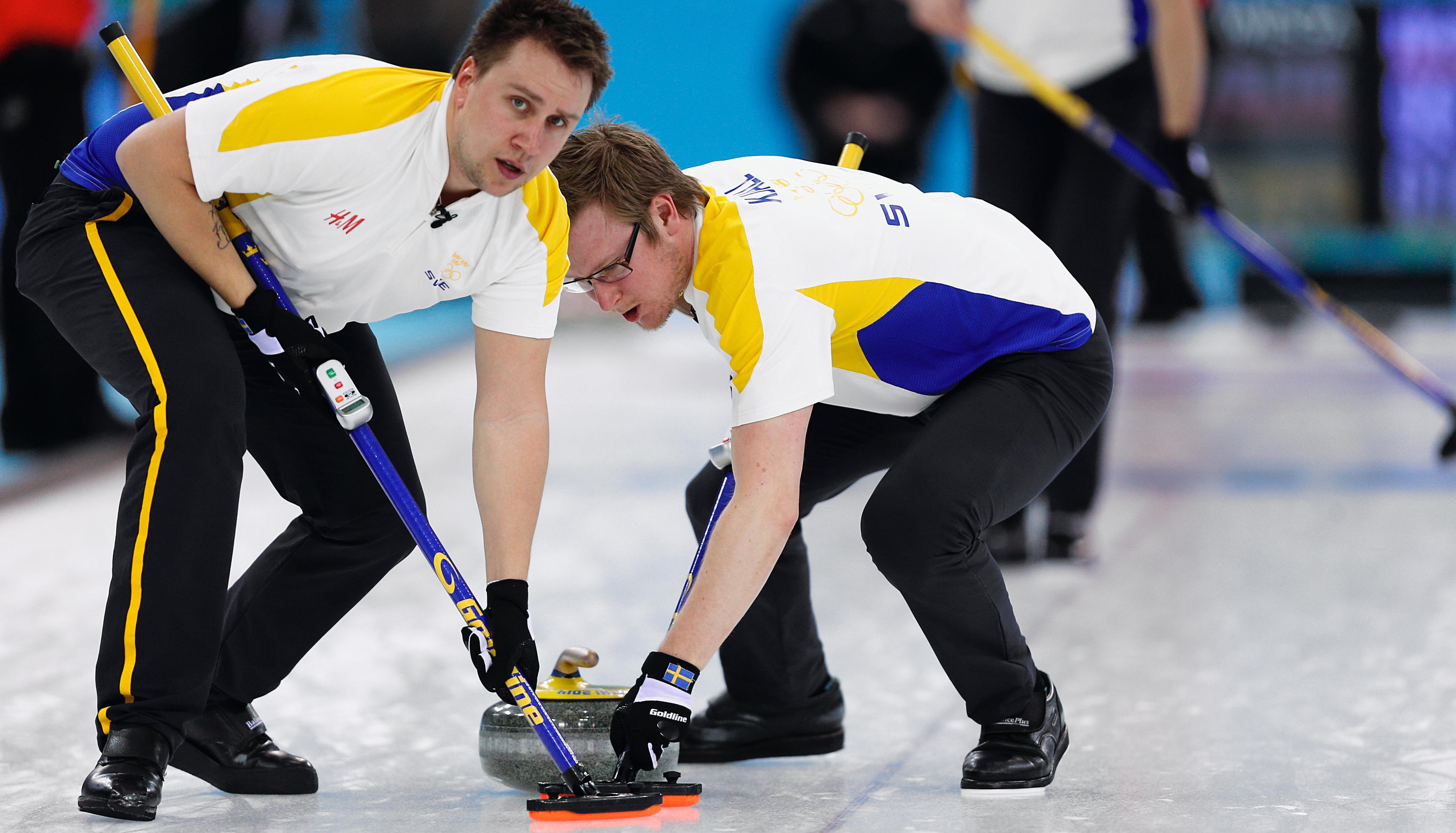 Two curlers on the ice in a competition with the broomsticks in front of the curling-stone.