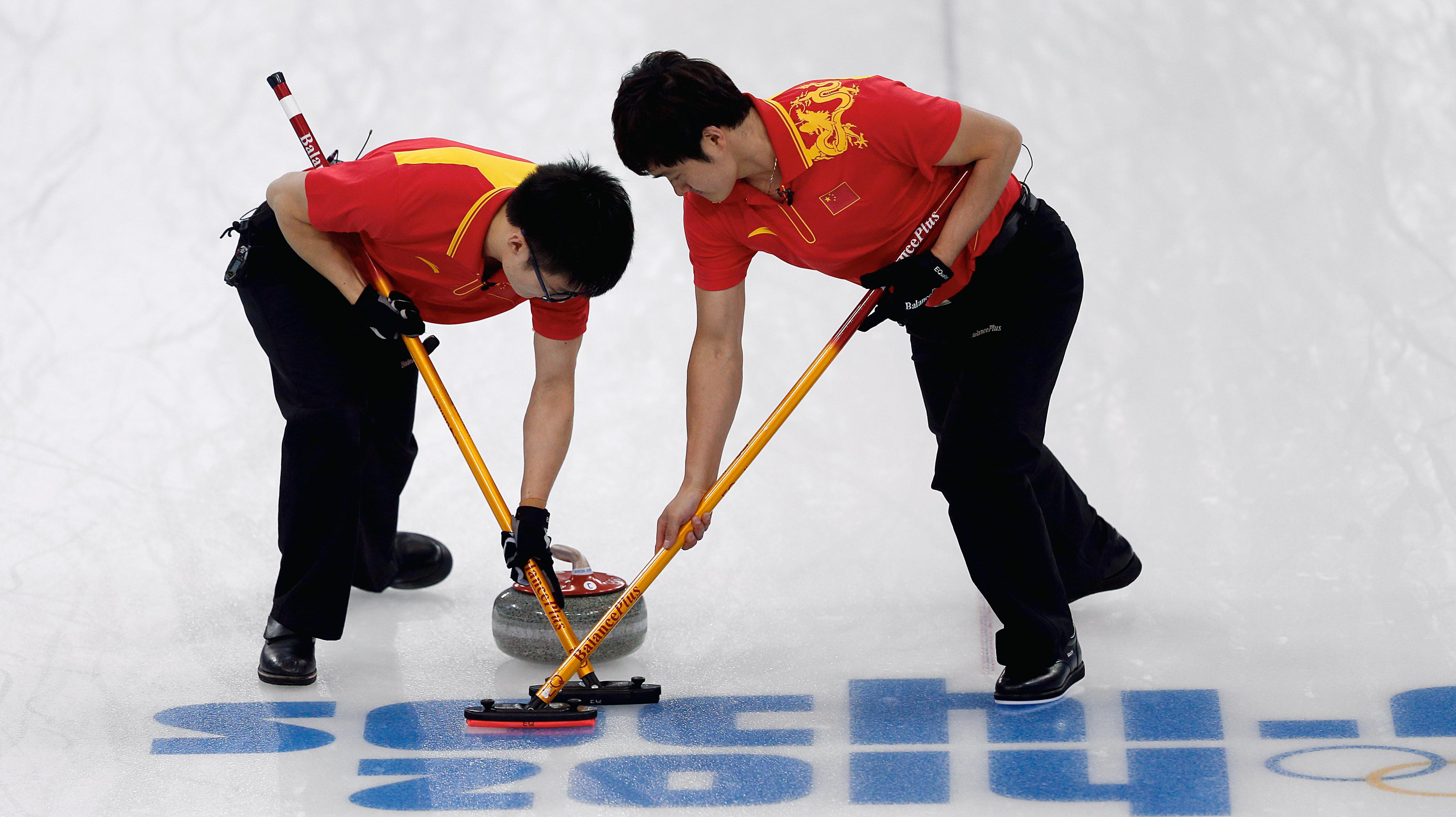 Two curlers on the ice in a competition using the broomsticks in front of the curling-stones.