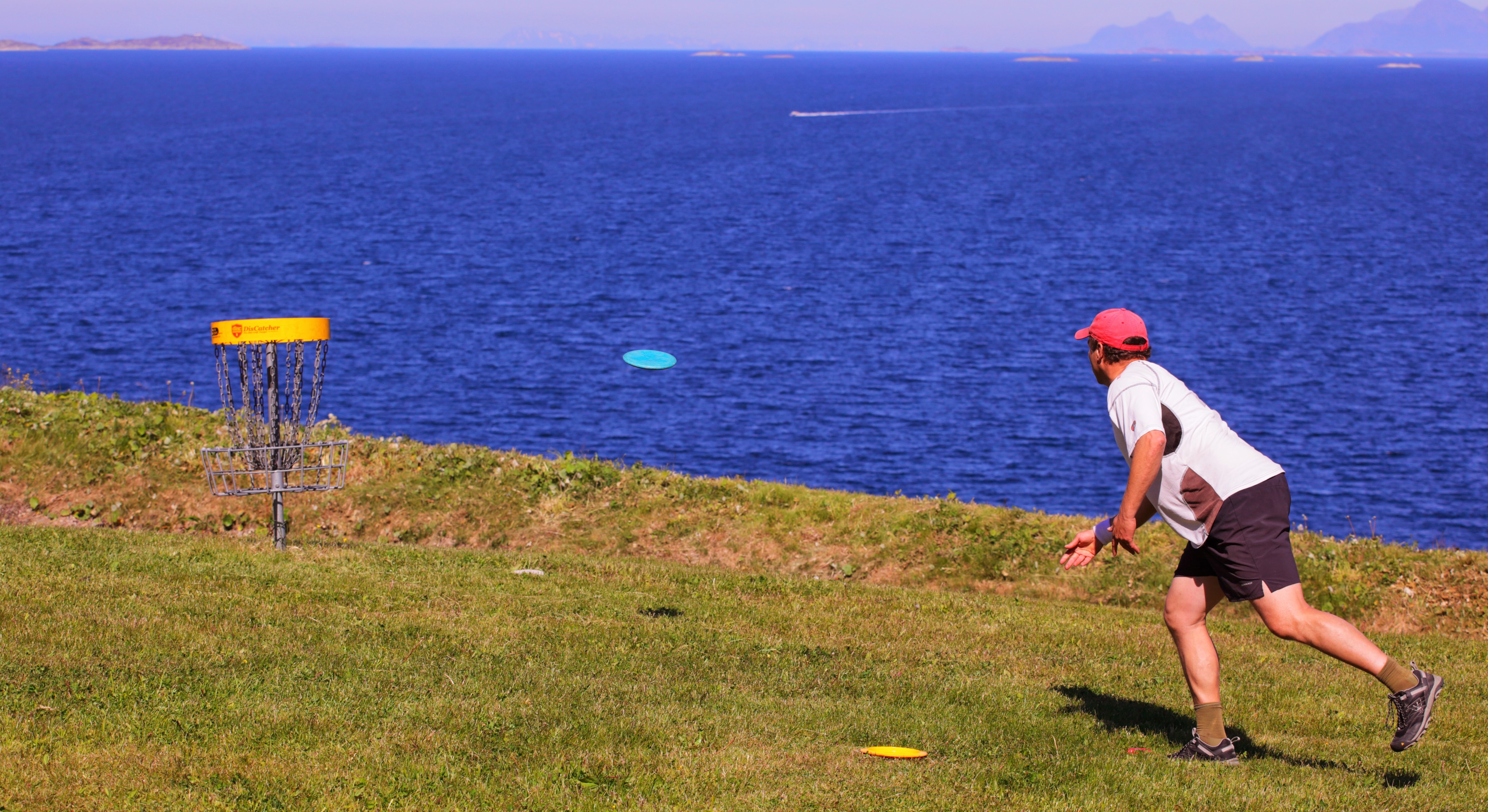 Athlete aiming and throwing the disc towards the disc-basket. The sea in the background.