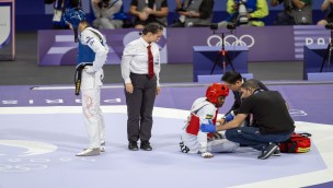Athletes in a taekwondo match and one is sitting on the court getting assistant from medical personell. 