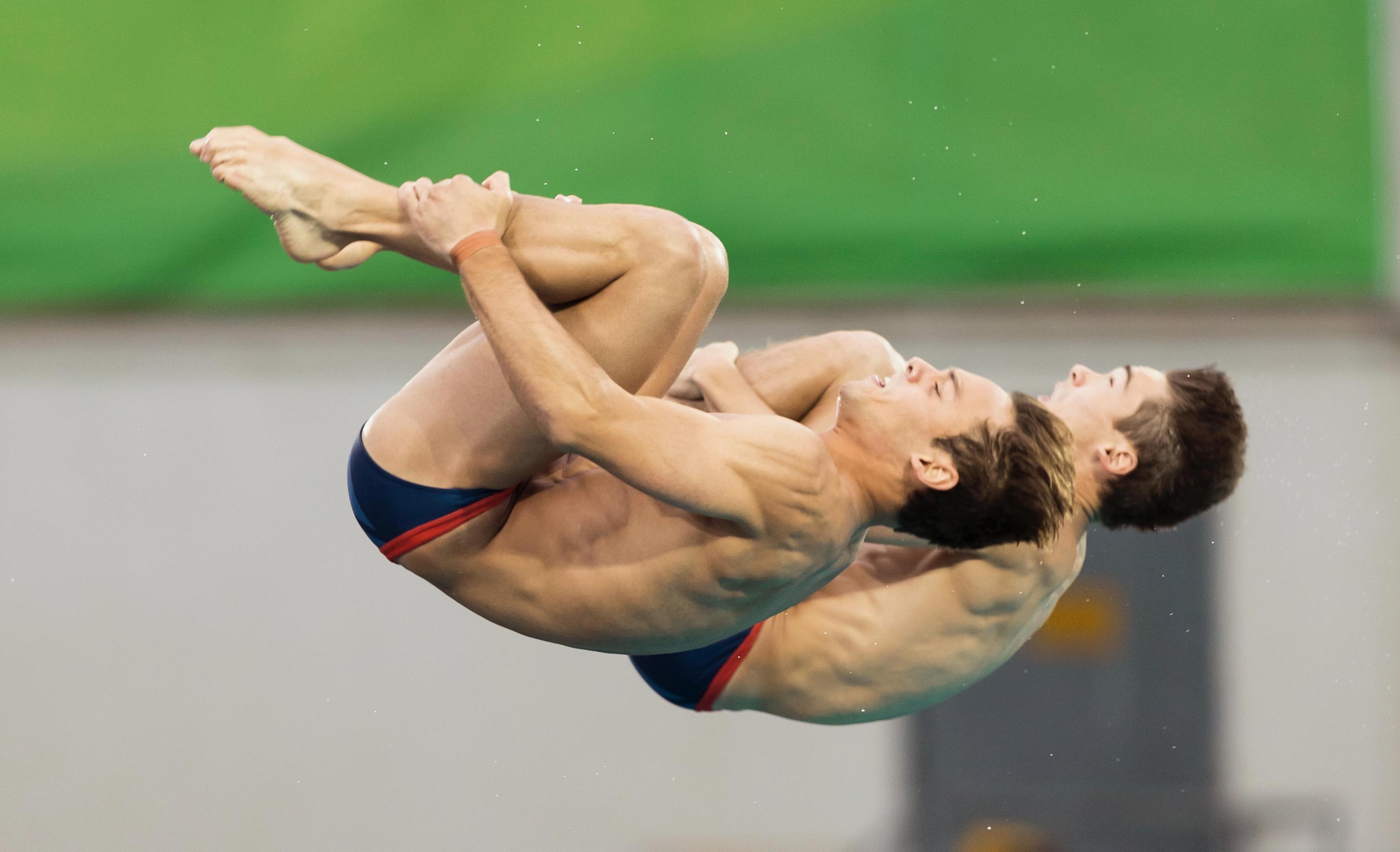 Two syncronized divers in the air, arms and legs togethe, doing a backflip in the air.