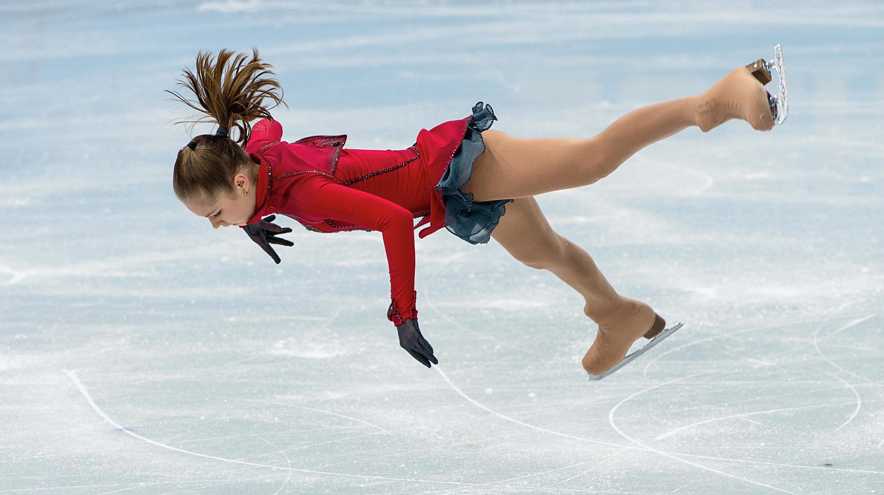 Figure skater on the ice, jumping up and are almosy lying vertical in the air.