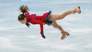 Figure skater on the ice, jumping up and are almosy lying vertical in the air. 