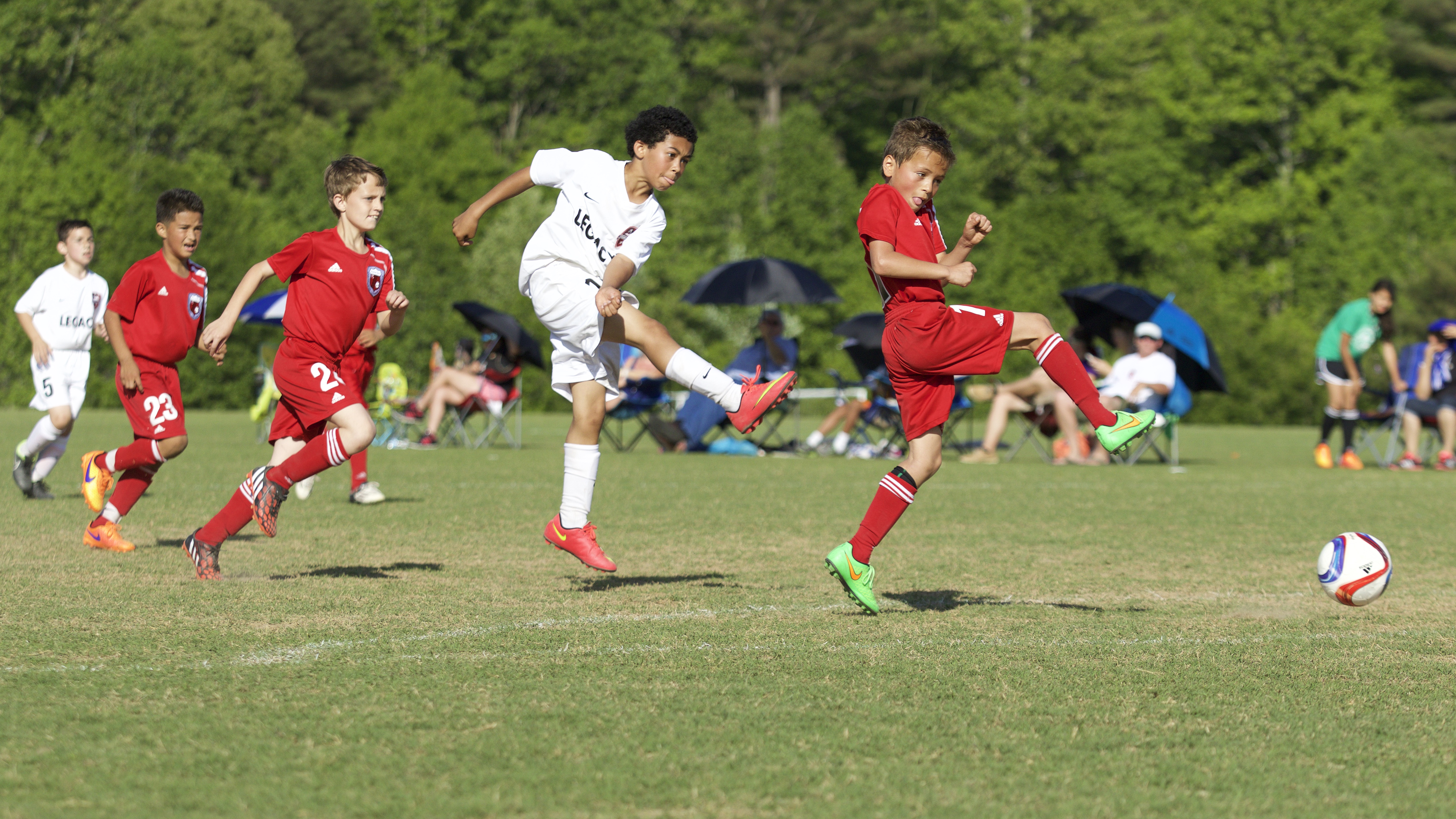 Several youth football players on the field, one of them in the air after just kicking the ball.