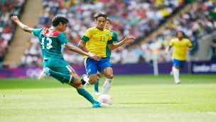 Several football players on the field, one player is just to kick the ball with his right leg, while an opponent is right in front of him.