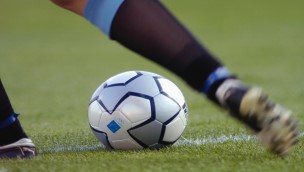 Close up of a football on the field, where a player is getting ready to kick the ball, only seing the players leg.