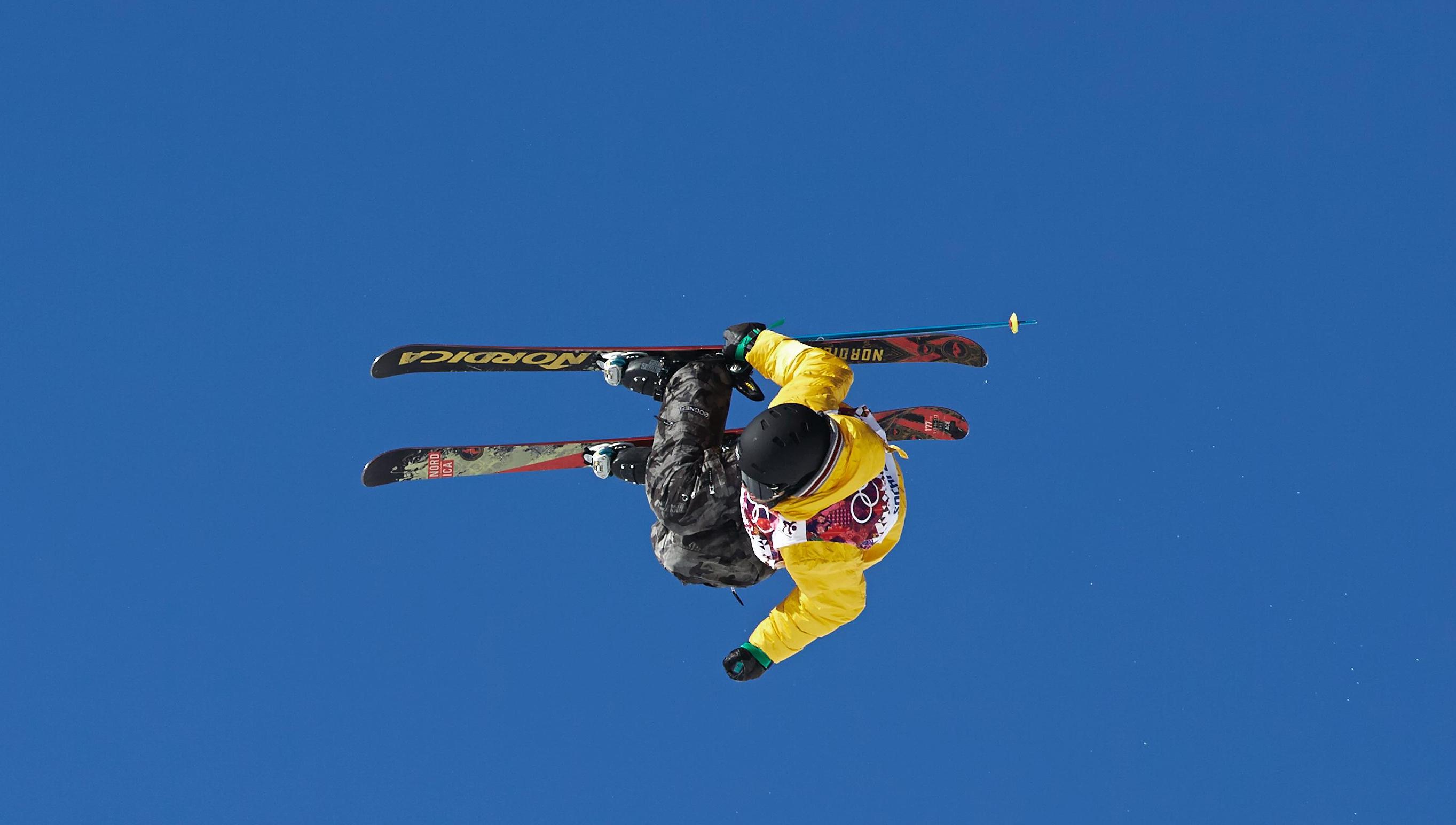 Freeskier in the air lying a bit on the side, blue sky in the background.
