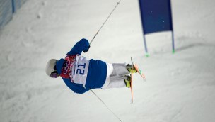 Freeskier seen from behind in the slope, having just did a jump and are flying in the air while being tilted a bit to the side.