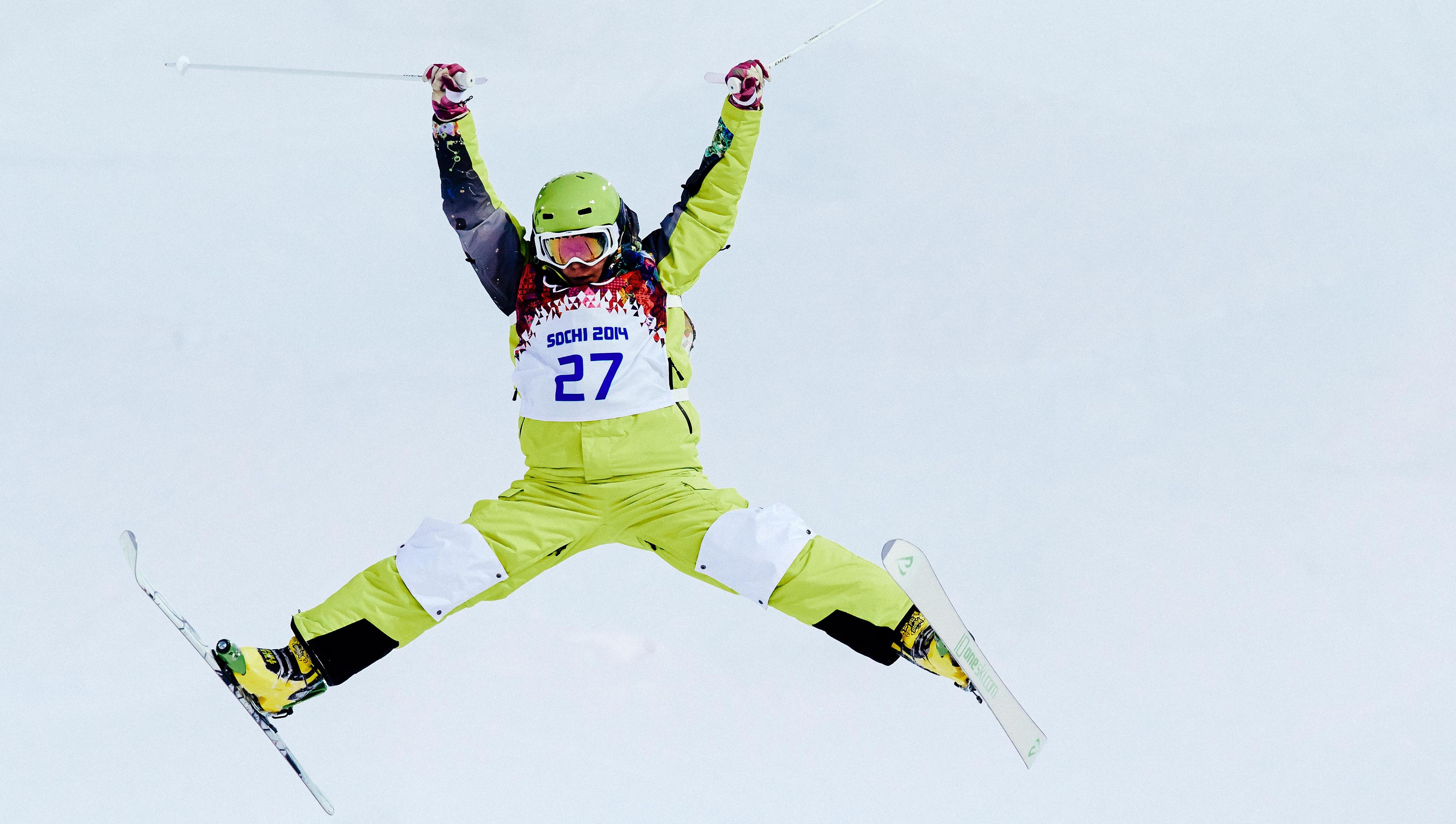 Mogul skier in a competition, in the air, arms and legs out to the side in a "star" formation.