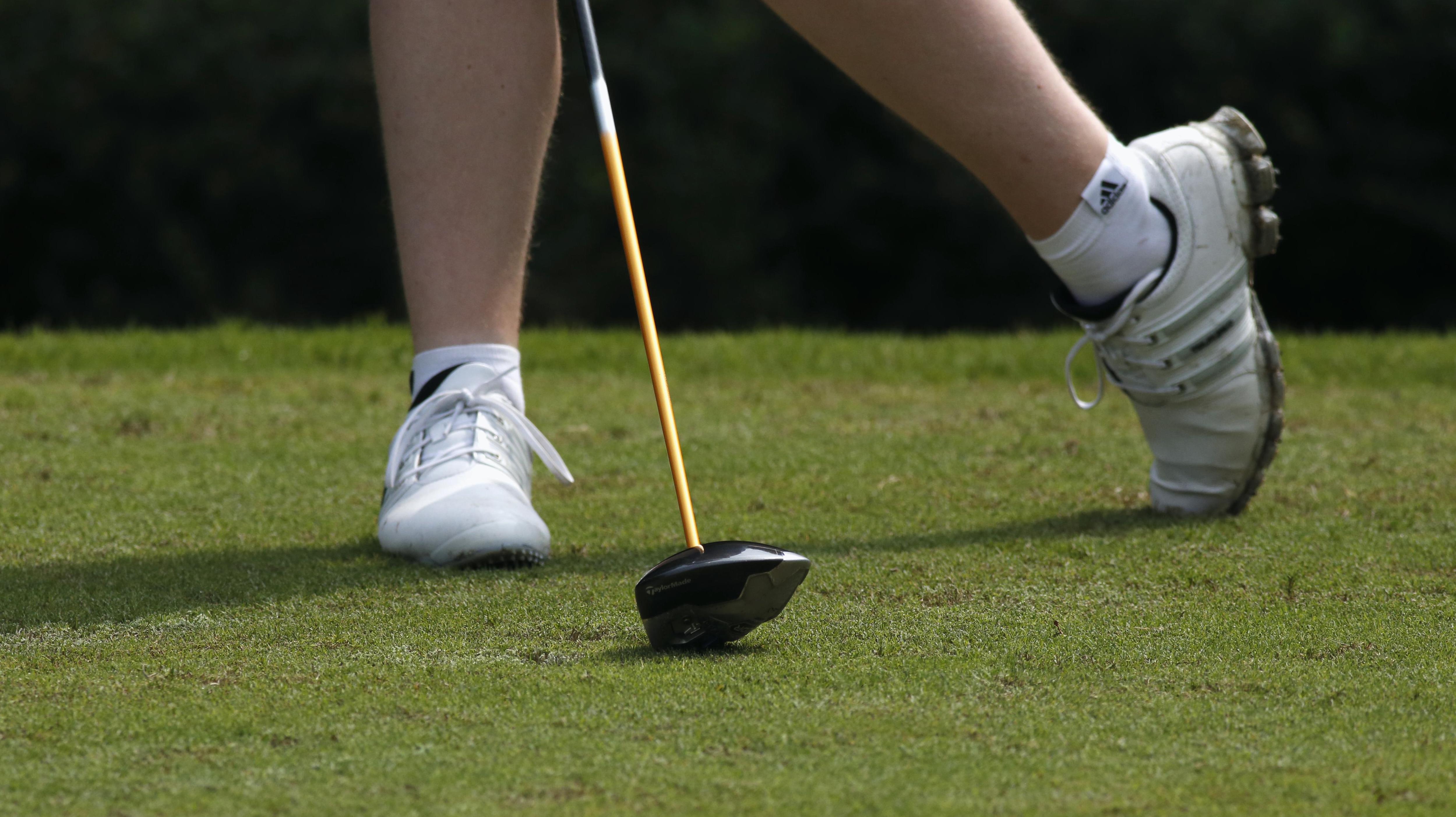 Close up of a gold club on the gras, also seeing some feet in the background.