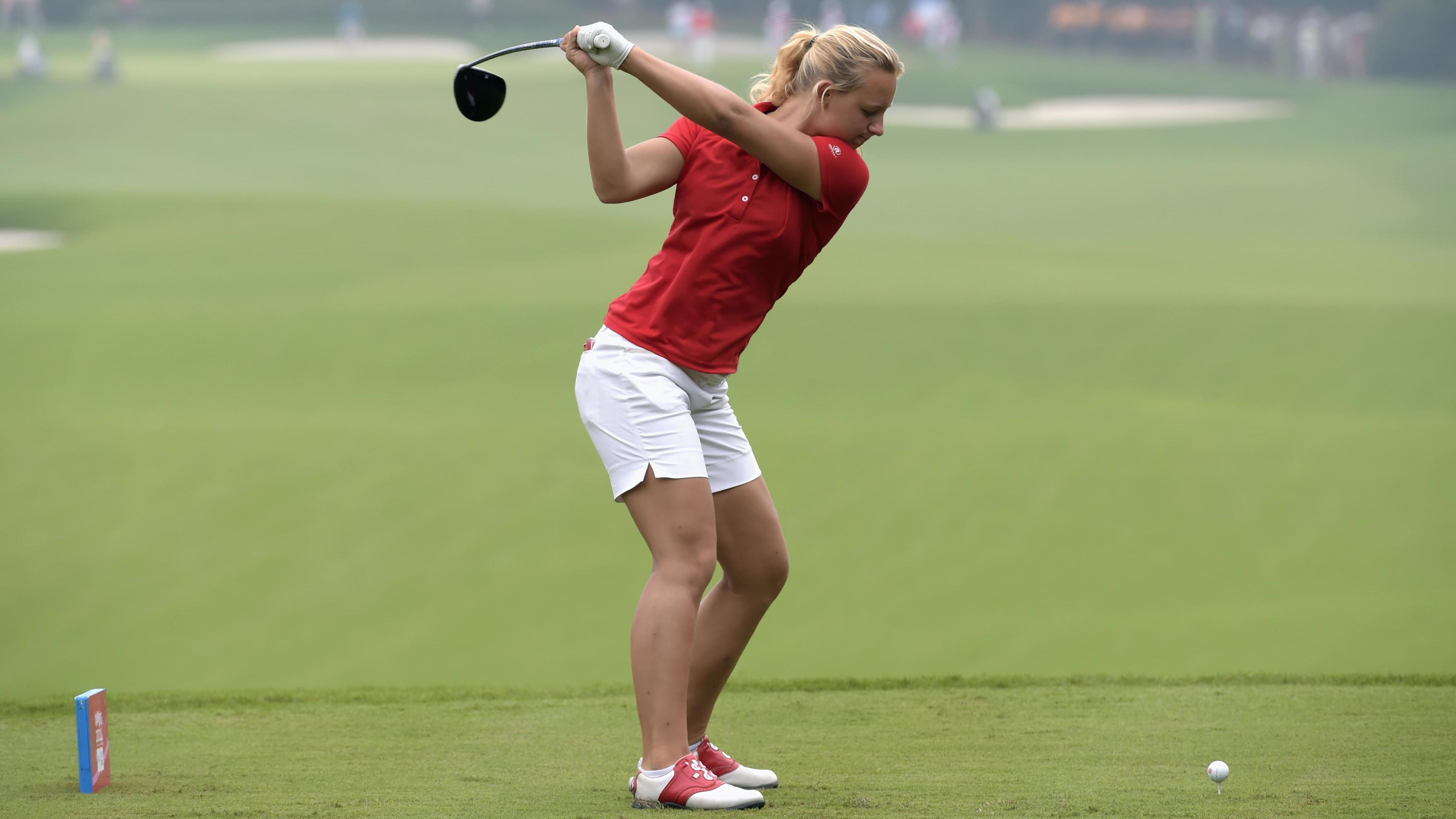 Golf player ready to hit the ball on the gras. She has her golfclub lifted, ready to swing.