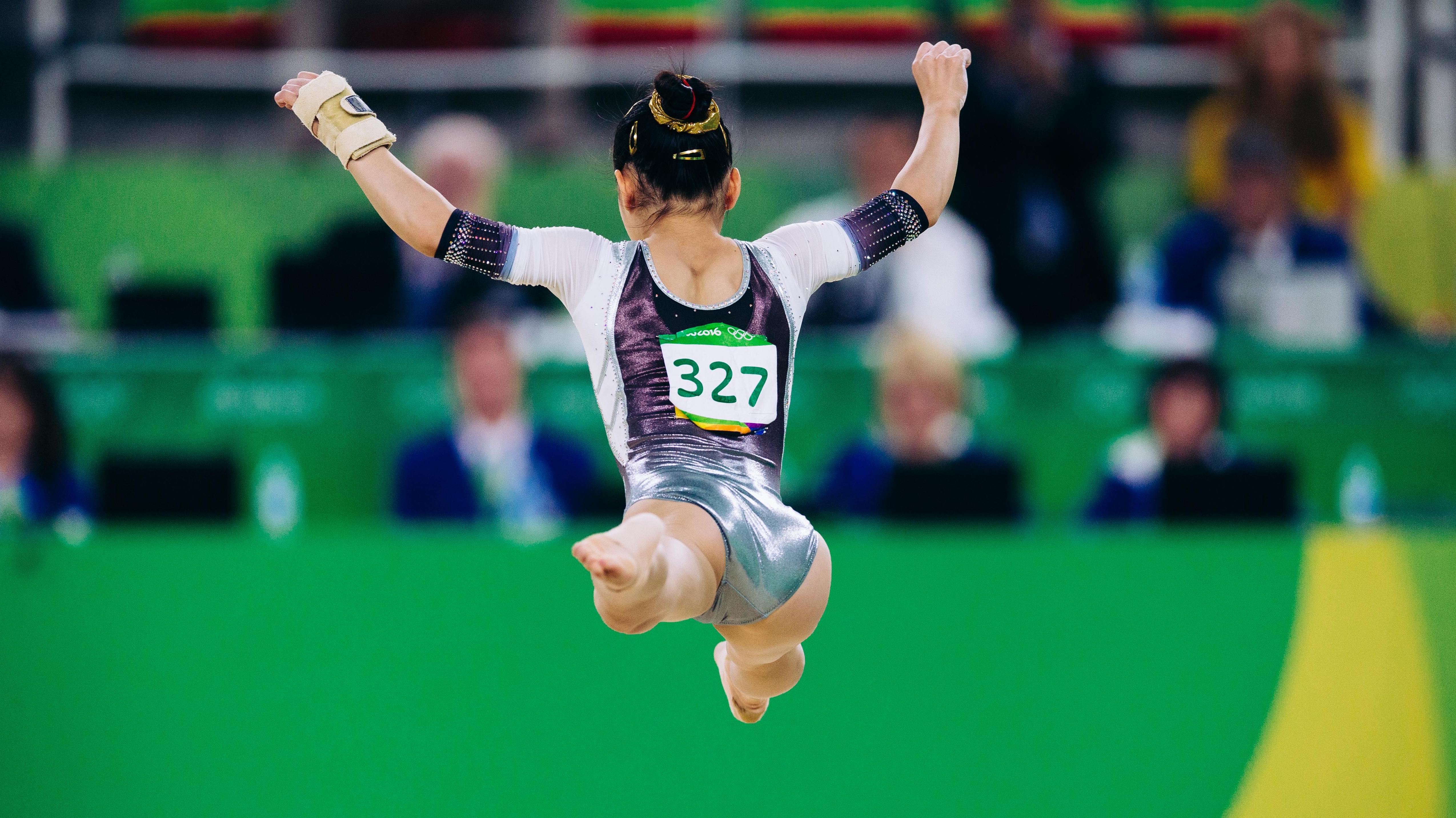 Gymnast in the air, seen from behind, doing the split.