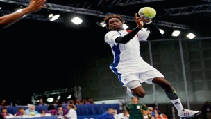 Handballplayer in the air with the ball in his right hand, looking forward towards the goalkeeper. 