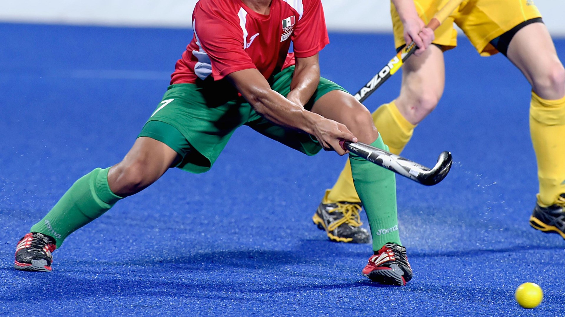 Close up of an athletes legs and feet with his hockeystick in the field, having just passed the ball. 