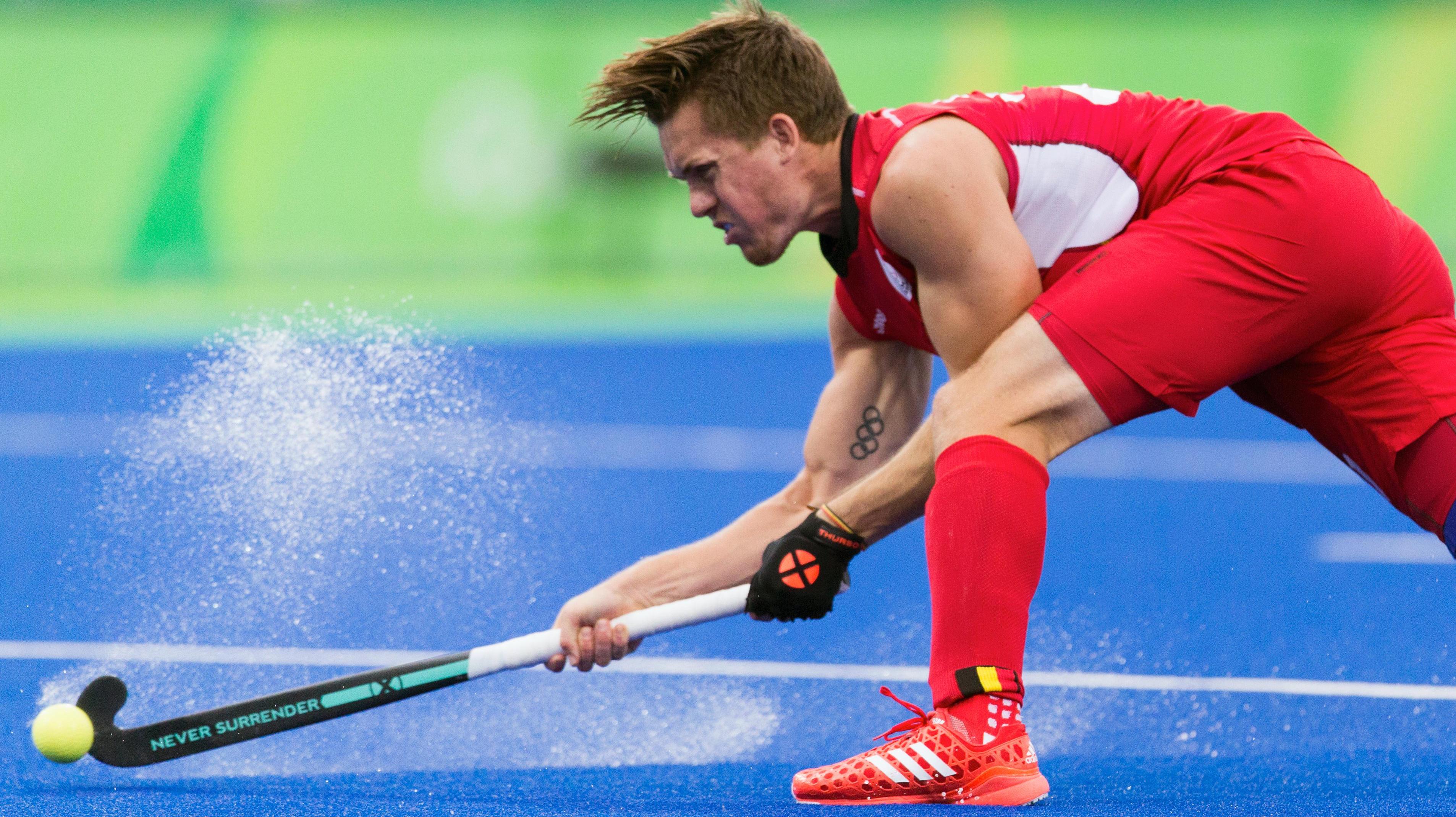 Athlete in the field, bending forward and making a shot with his hockeystick.