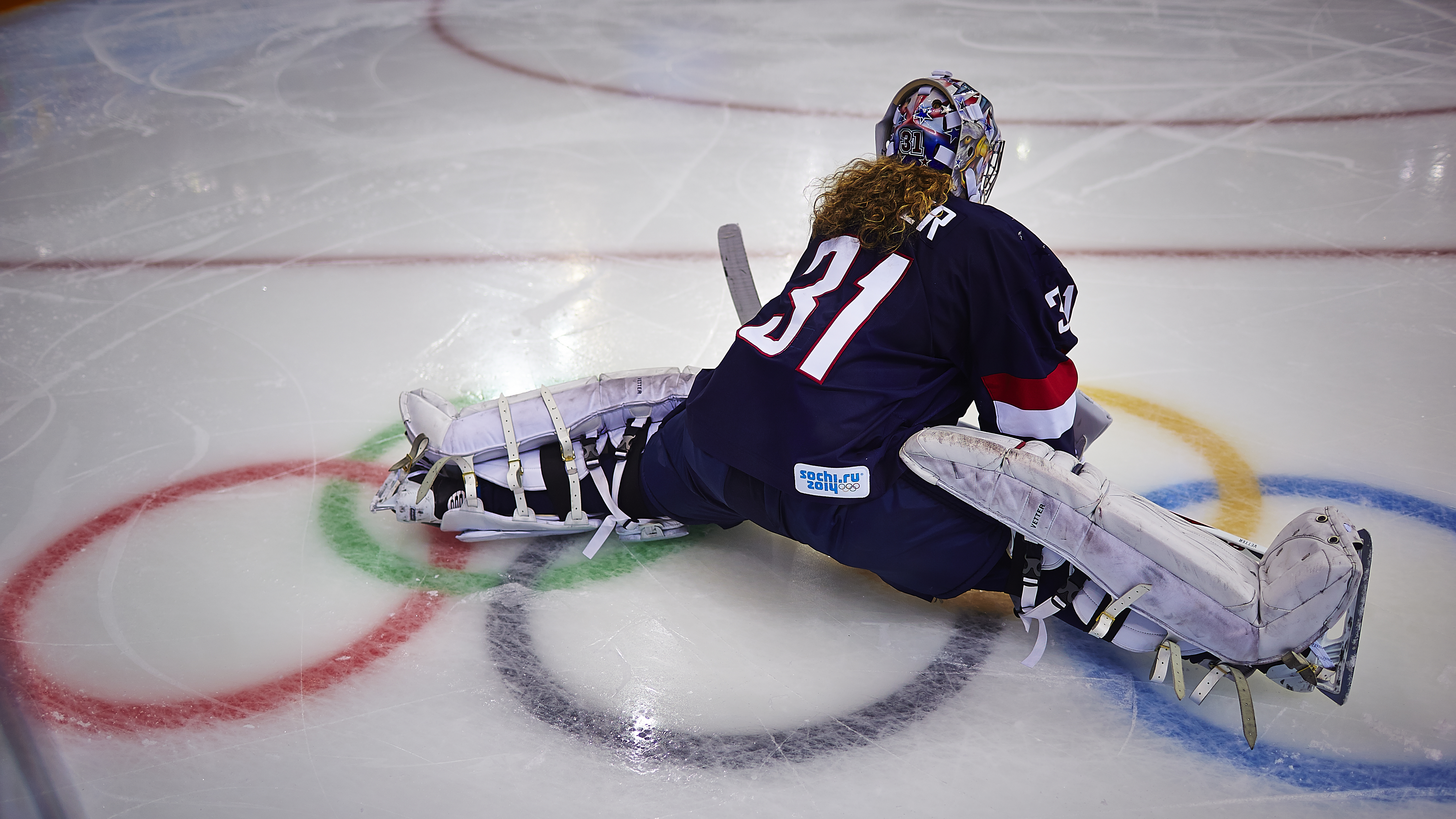 Ice-hocket goalkeeper on the ice seen from behind doing the split.