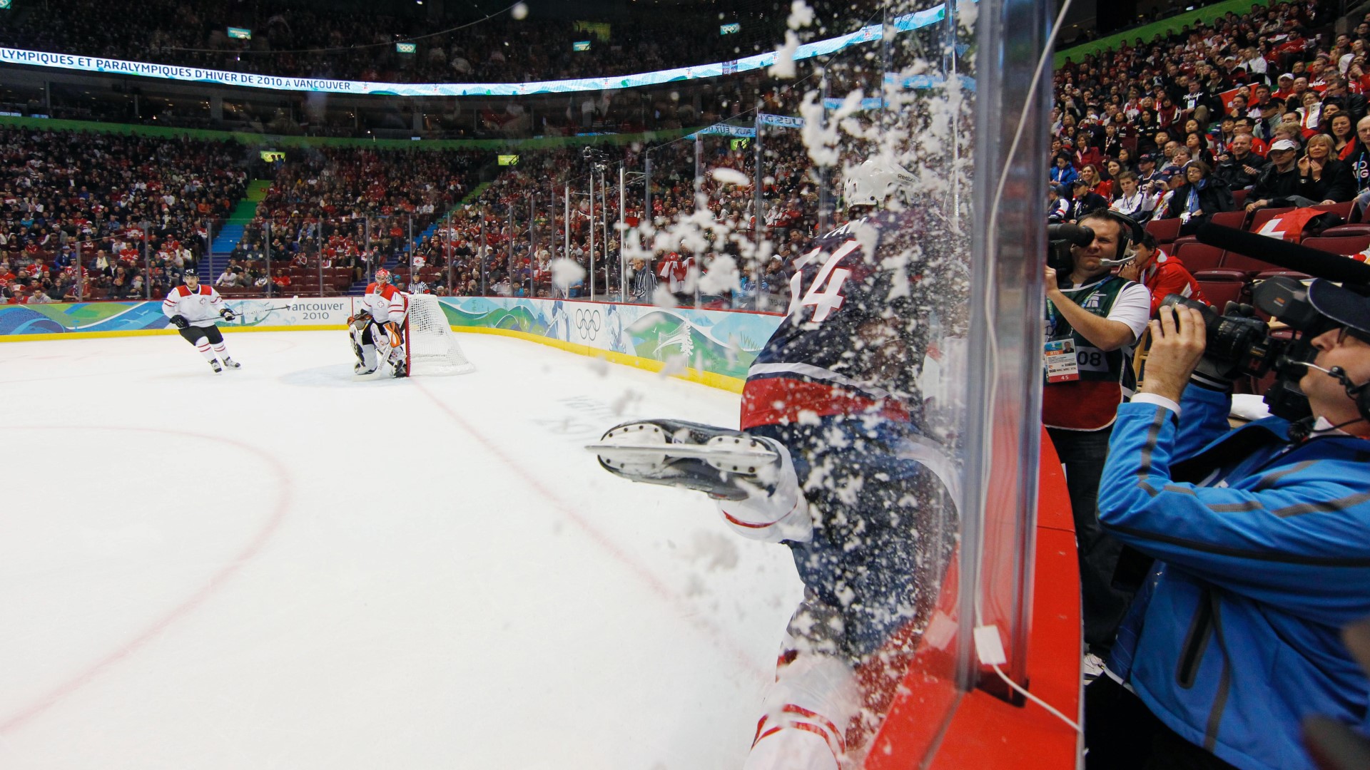 Ice-hockey player being pushed on the side agains the plexiglass in a match. Crowds around the whole stadium.