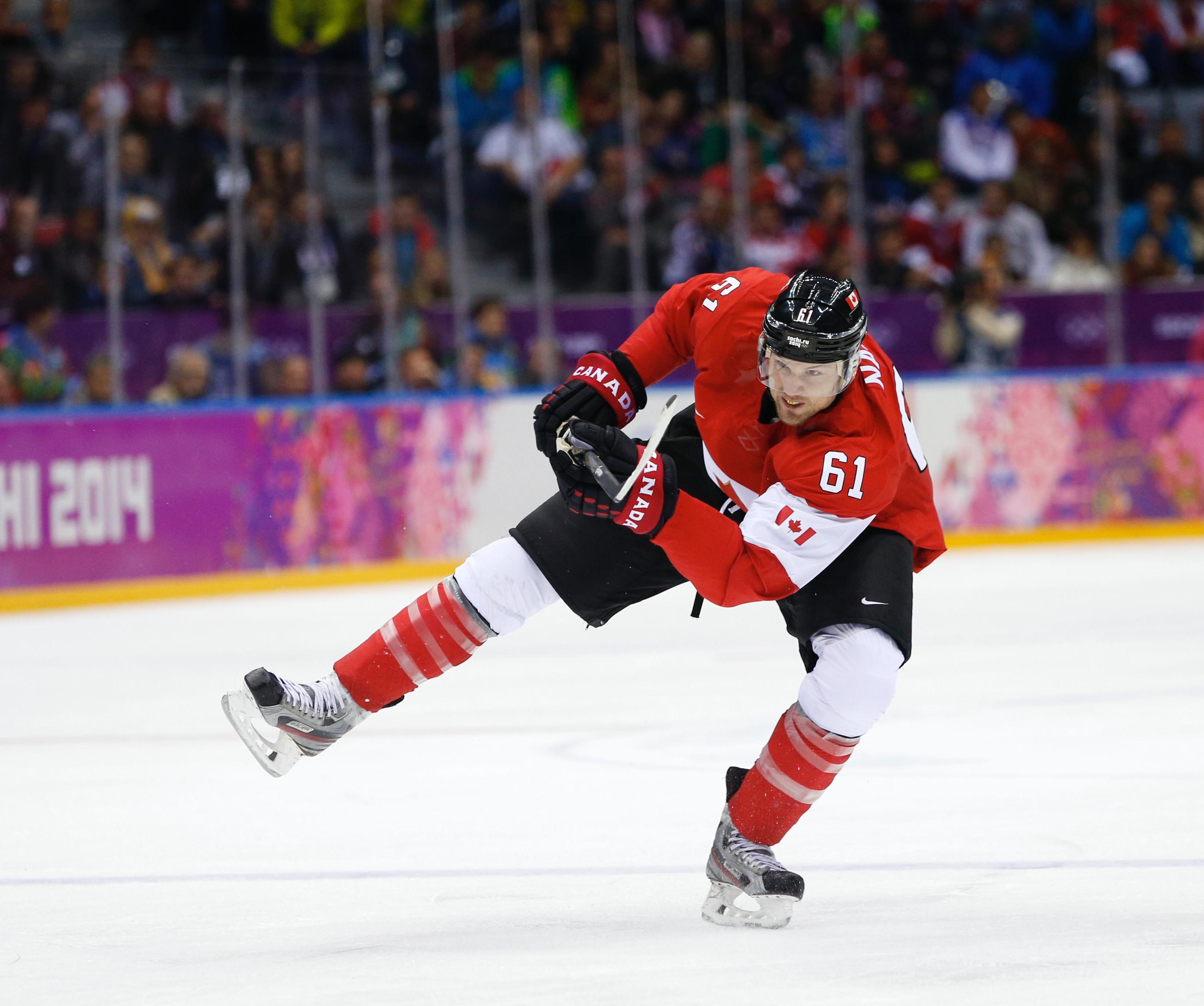 Ice-hockey player on the ice, standing on one leg and hitting the puck with his hockeystick.