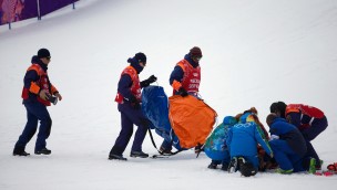 Several medical personell on the snow, going over to an athlete who is on the ground.