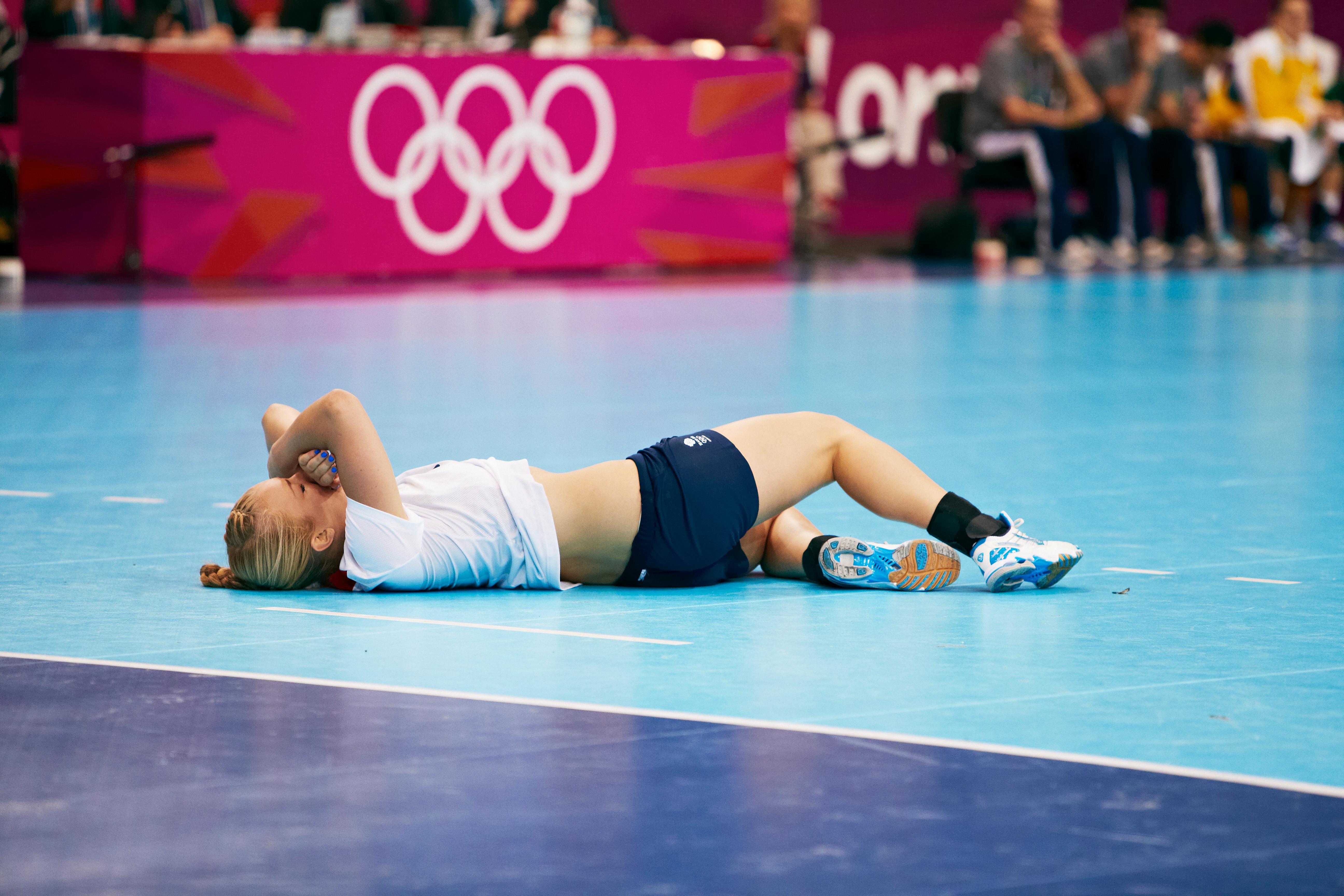 Handballplayer lying on the court with her arms over her face.