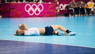 Handballplayer lying on the court with her arms over her face.