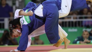 Two athletes in a Judo competition in close combat, both holding onto each other and on the way down on the ground.