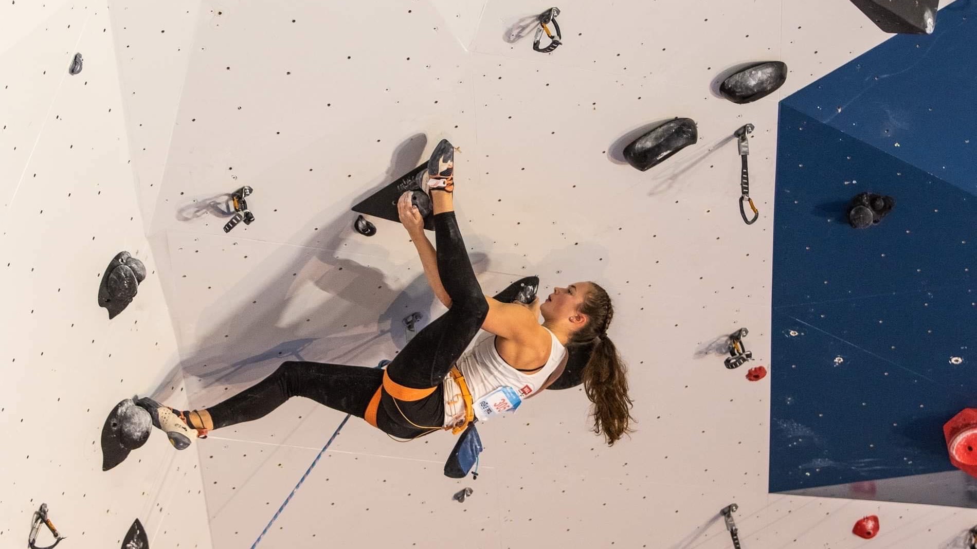 Climber in a climbing wall inndoor, almost hanging up-side down.
