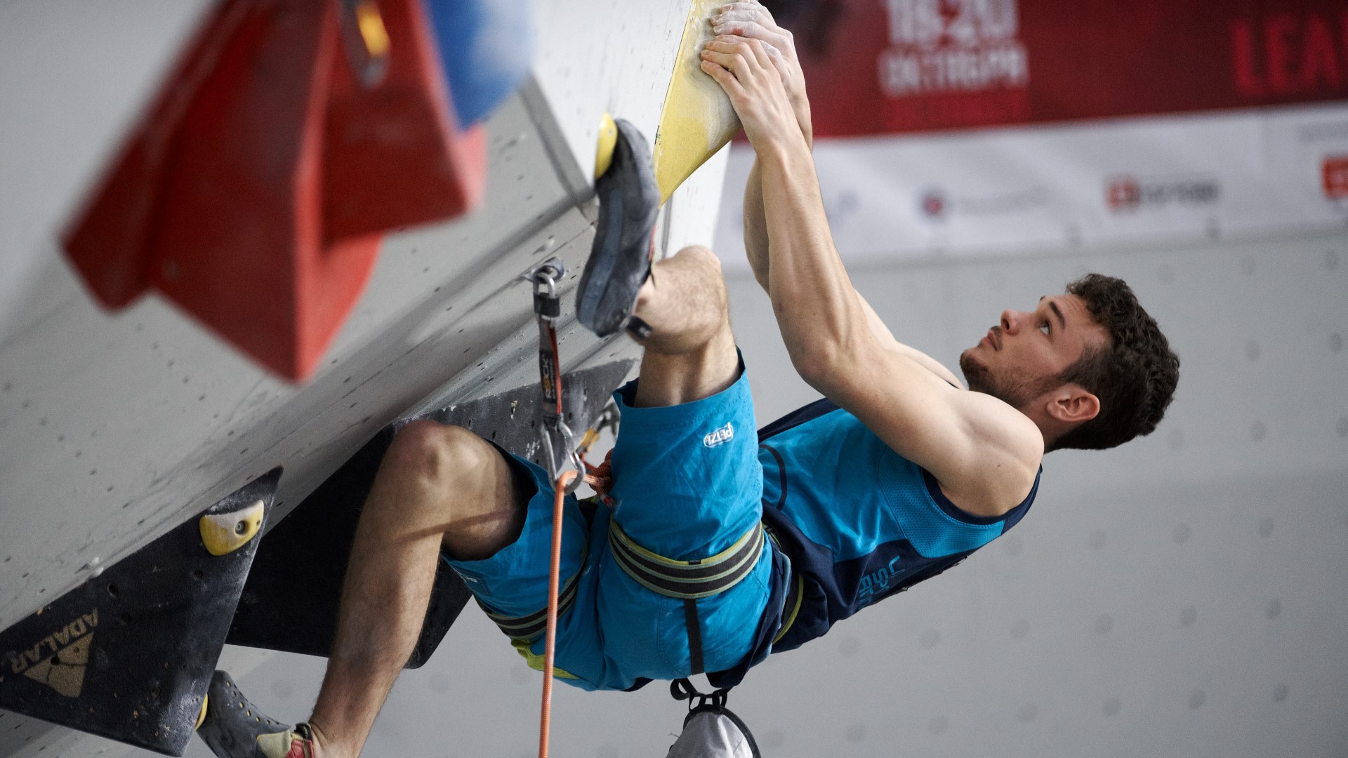 Man climbing indoor, hanging almost upside down.