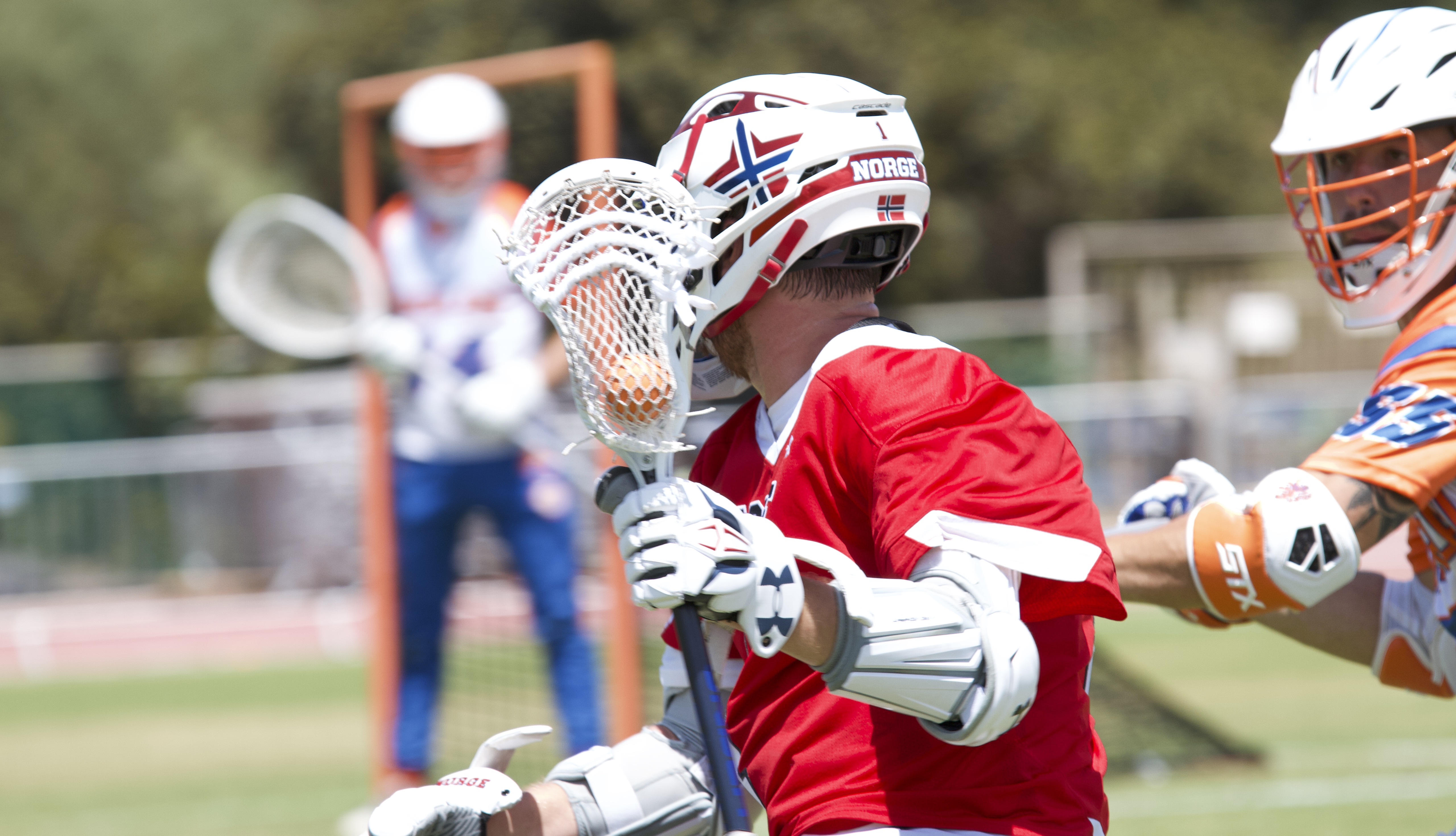 Lacrosse player seen from the side, holding his racket in fron of his face.